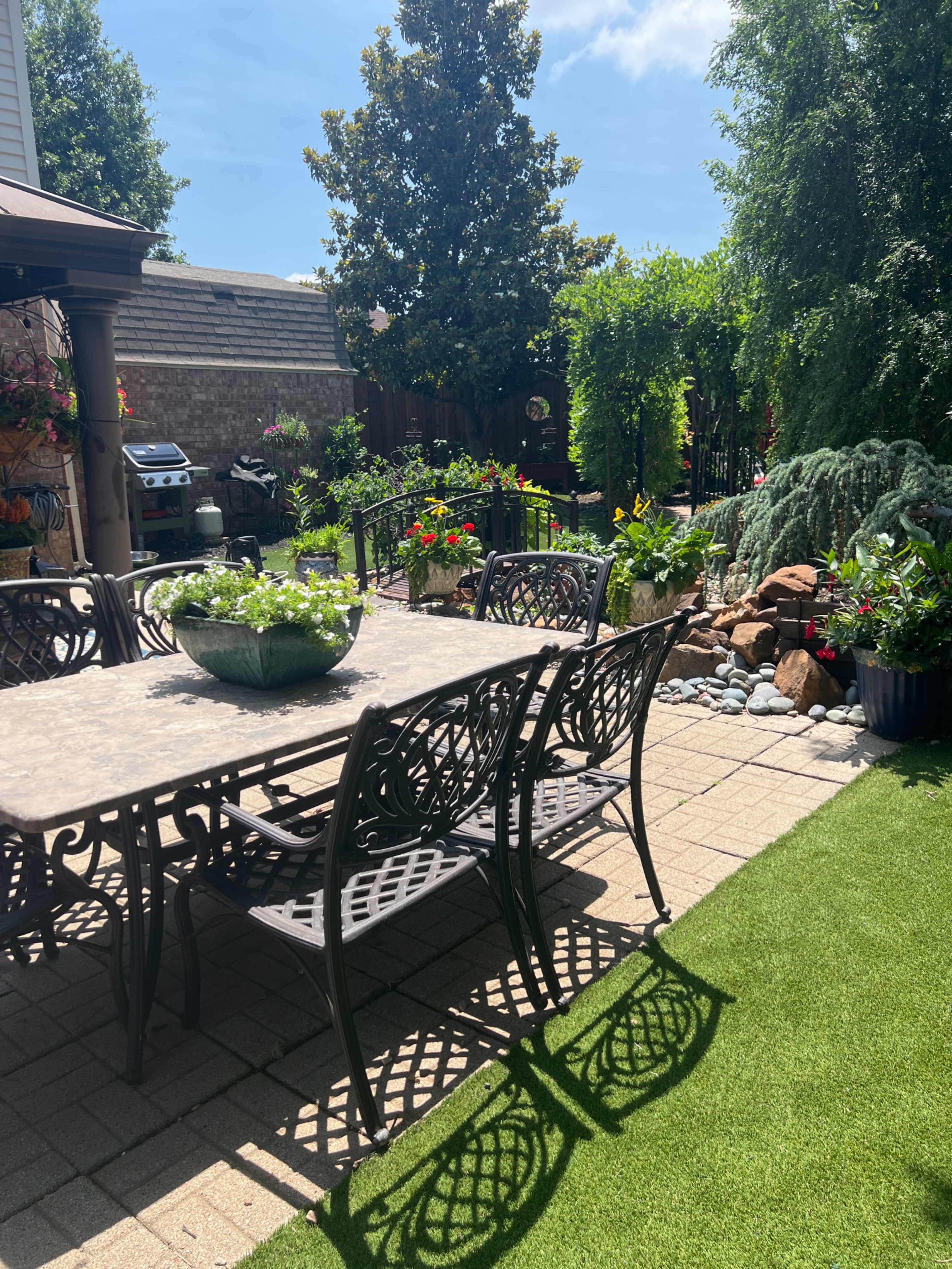 A patio area features a metal dining set surrounded by various plants and a small water feature.