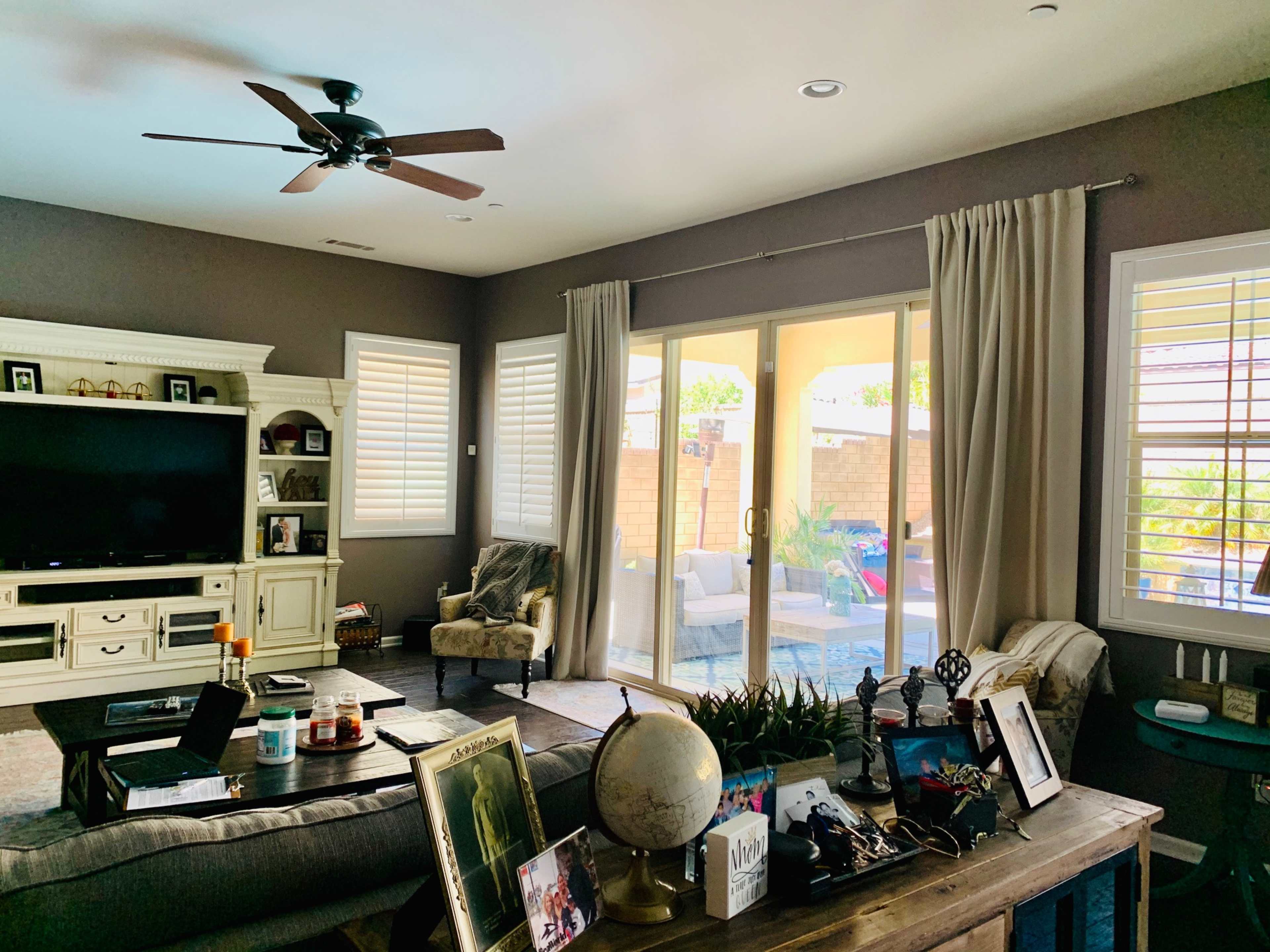 The living room features a television stand, a seating area with a chair, and a coffee table adorned with decorative items, while large sliding glass doors open to a backyard patio.