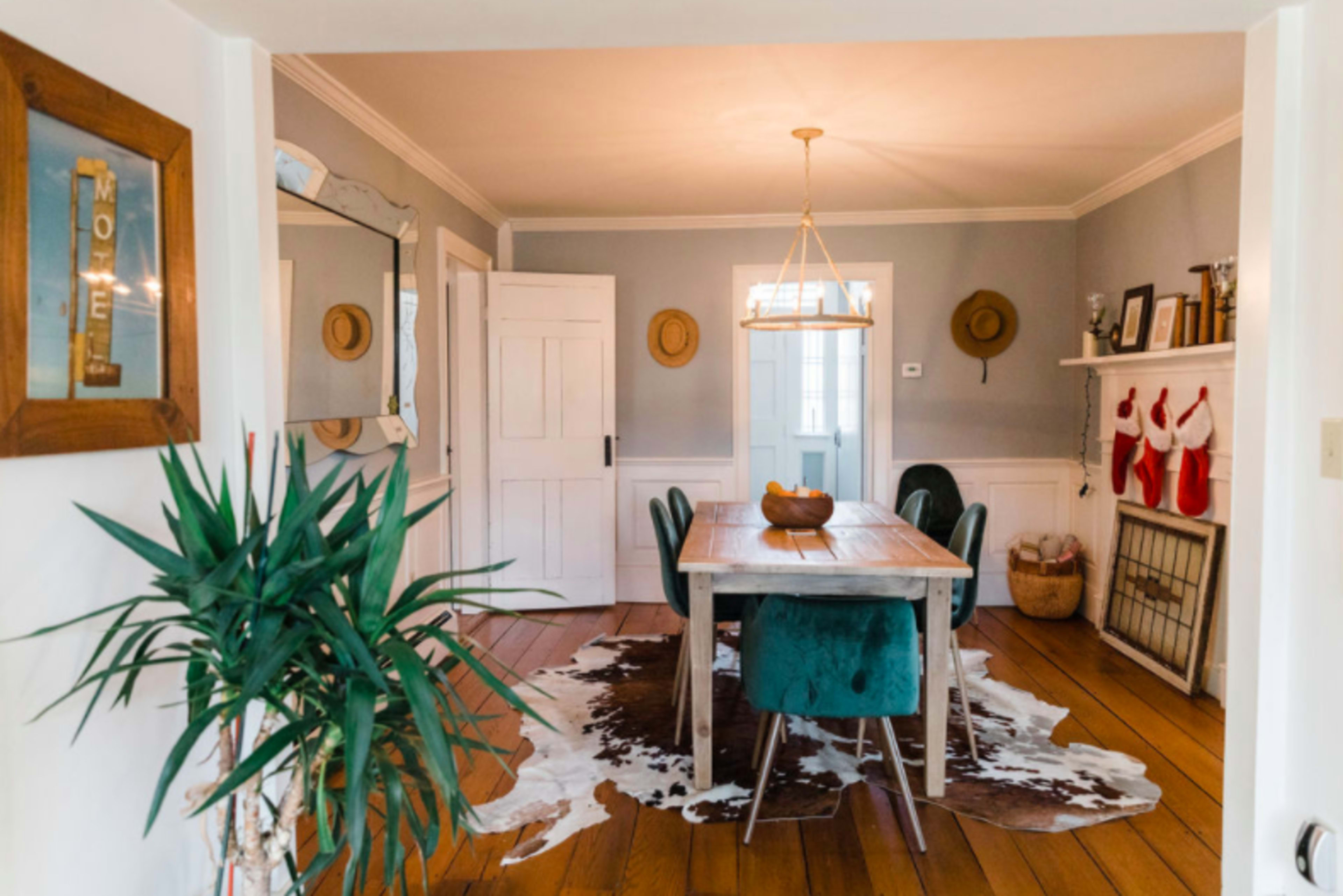 A dining room with a wooden table surrounded by teal chairs, a cowhide rug on the floor, and stockings hung by a fireplace.