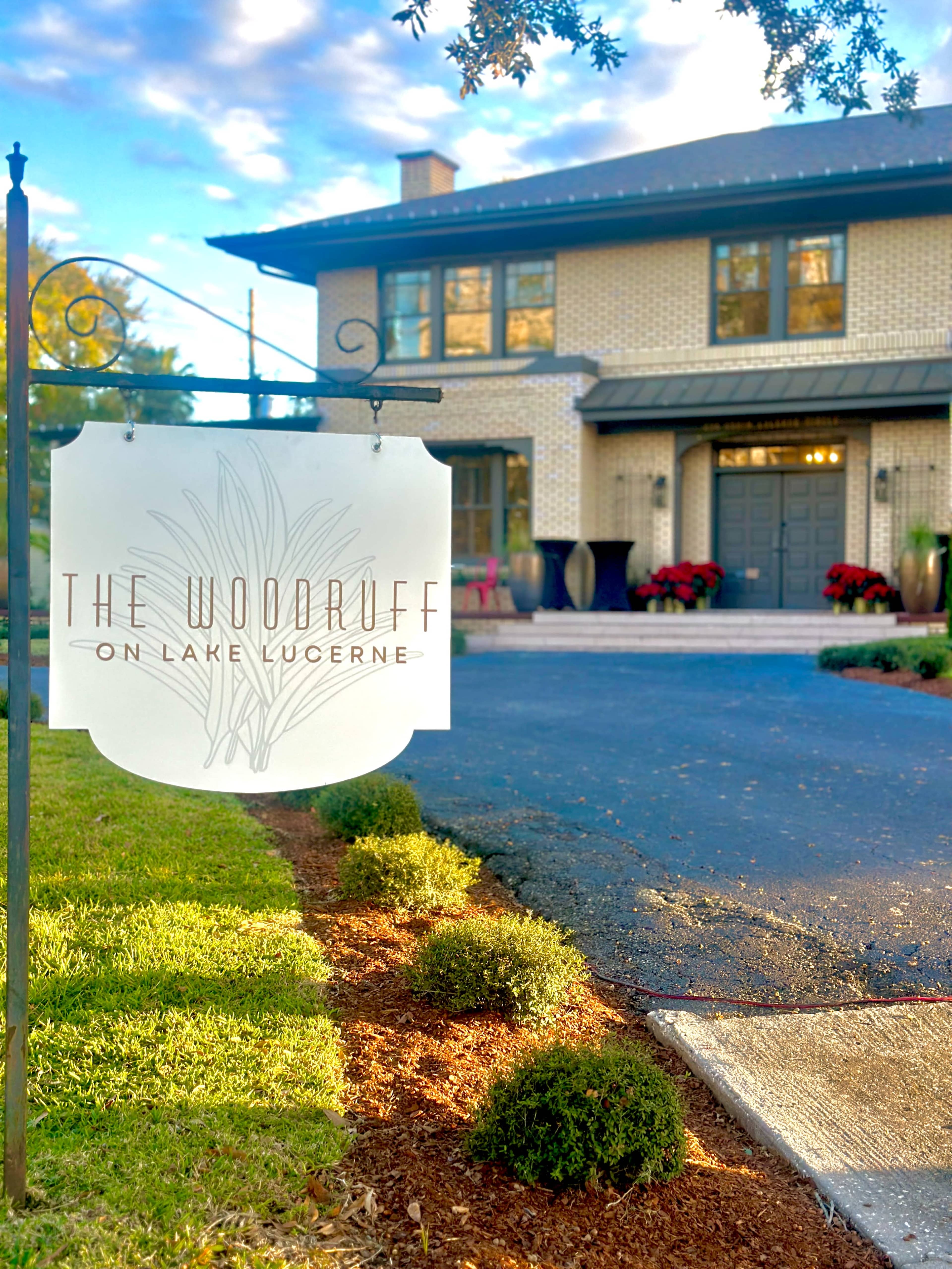 A sign reading "The Woodruff on Lake Lucerne" is displayed in front of a large, modern house with landscaped gardens and a paved driveway.