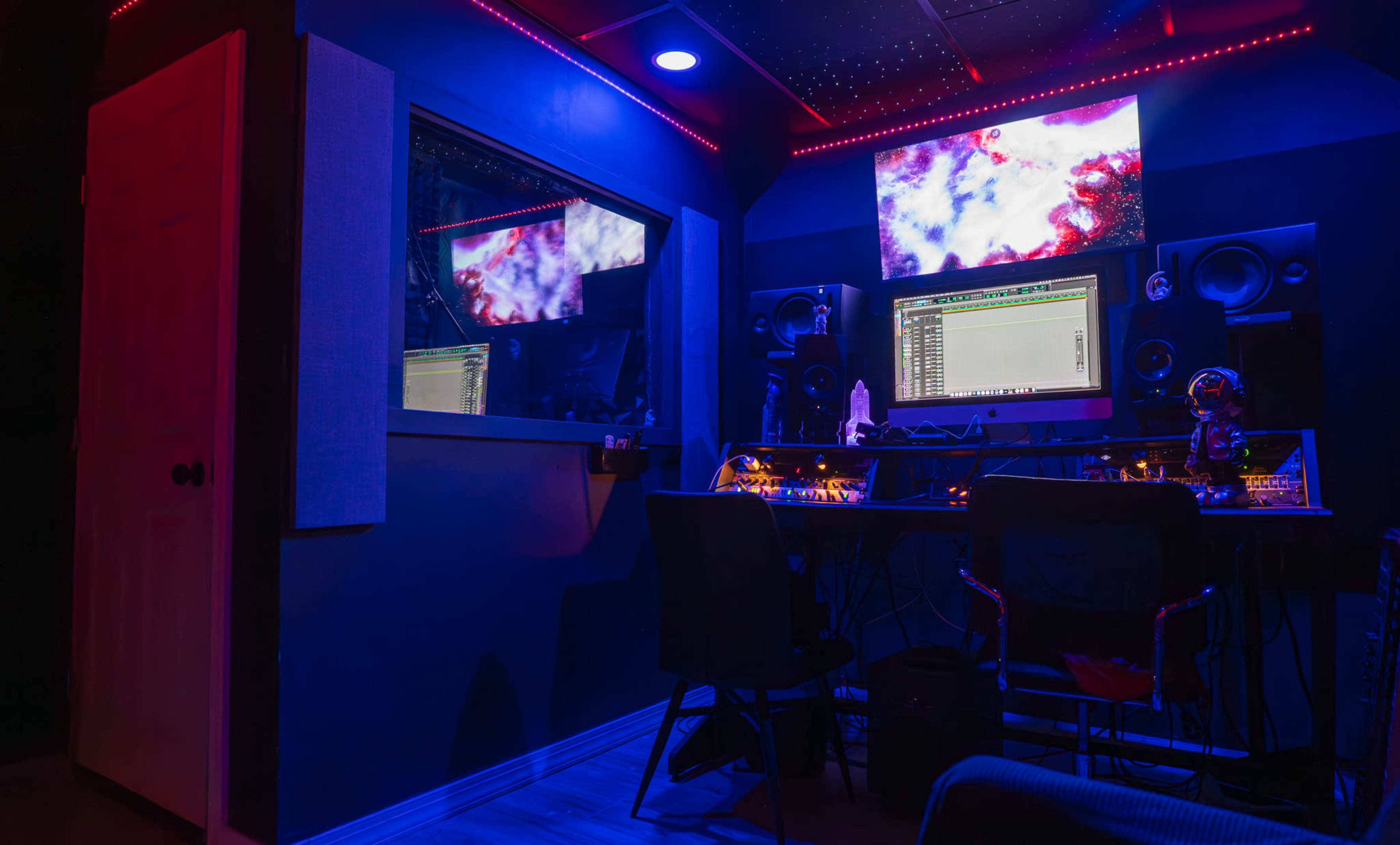 The image shows a music production studio with a large computer monitor, sound speakers, and colorful LED lights illuminating the room.