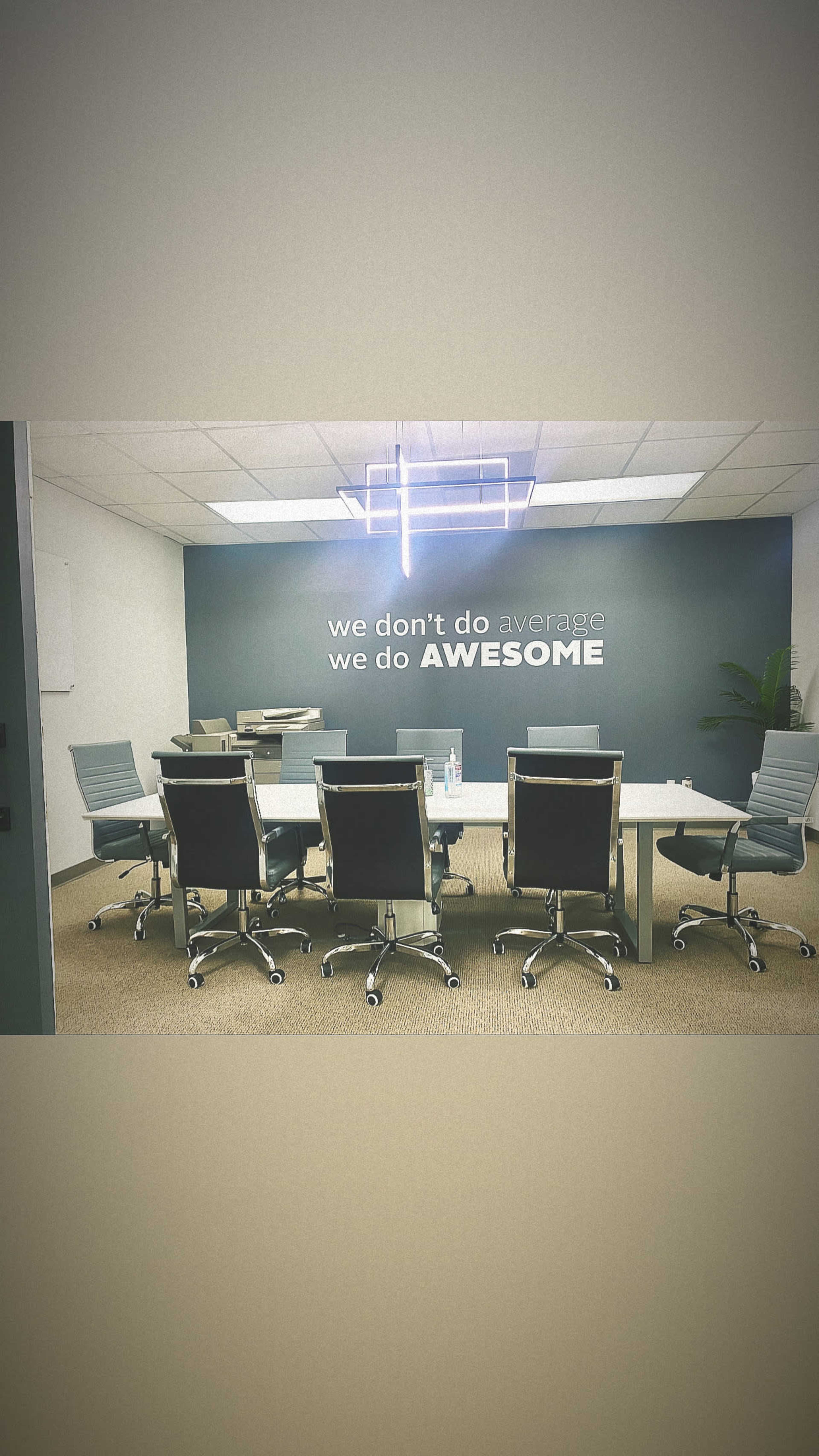 A modern conference room with a large table, several swivel chairs, and a wall featuring the quote "we don't do average we do AWESOME."