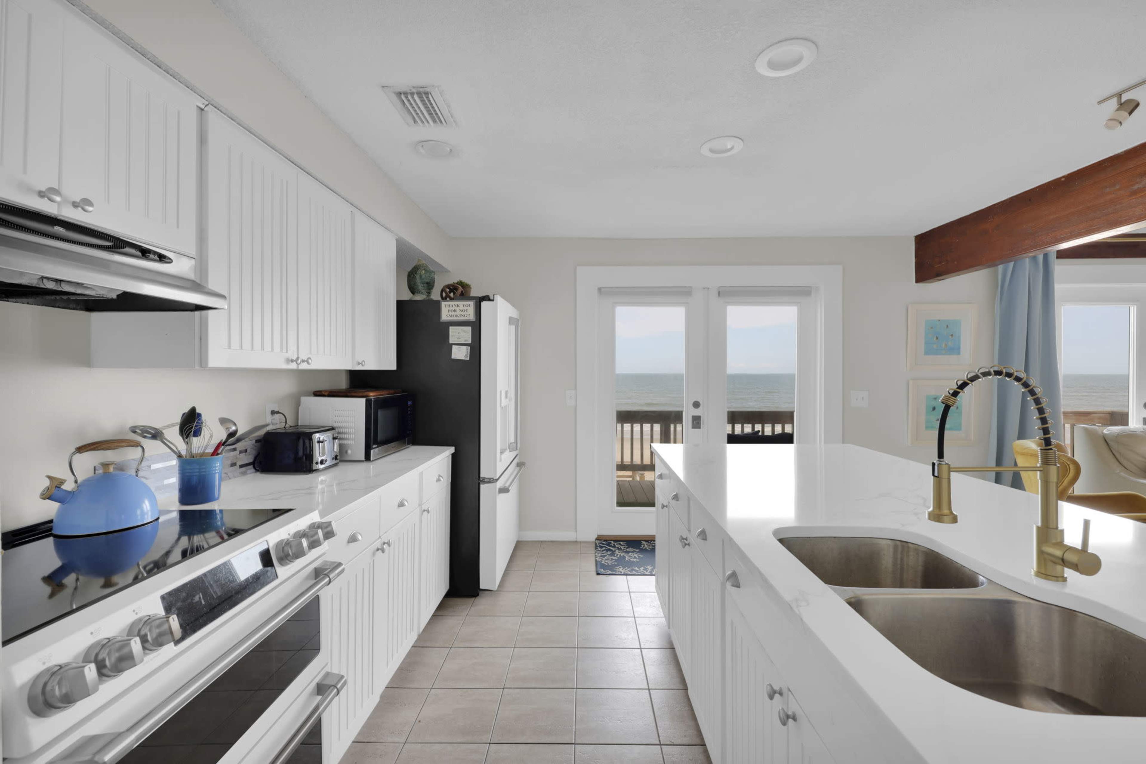 A modern kitchen featuring white cabinetry, stainless steel appliances, and a view of the ocean through sliding glass doors.
