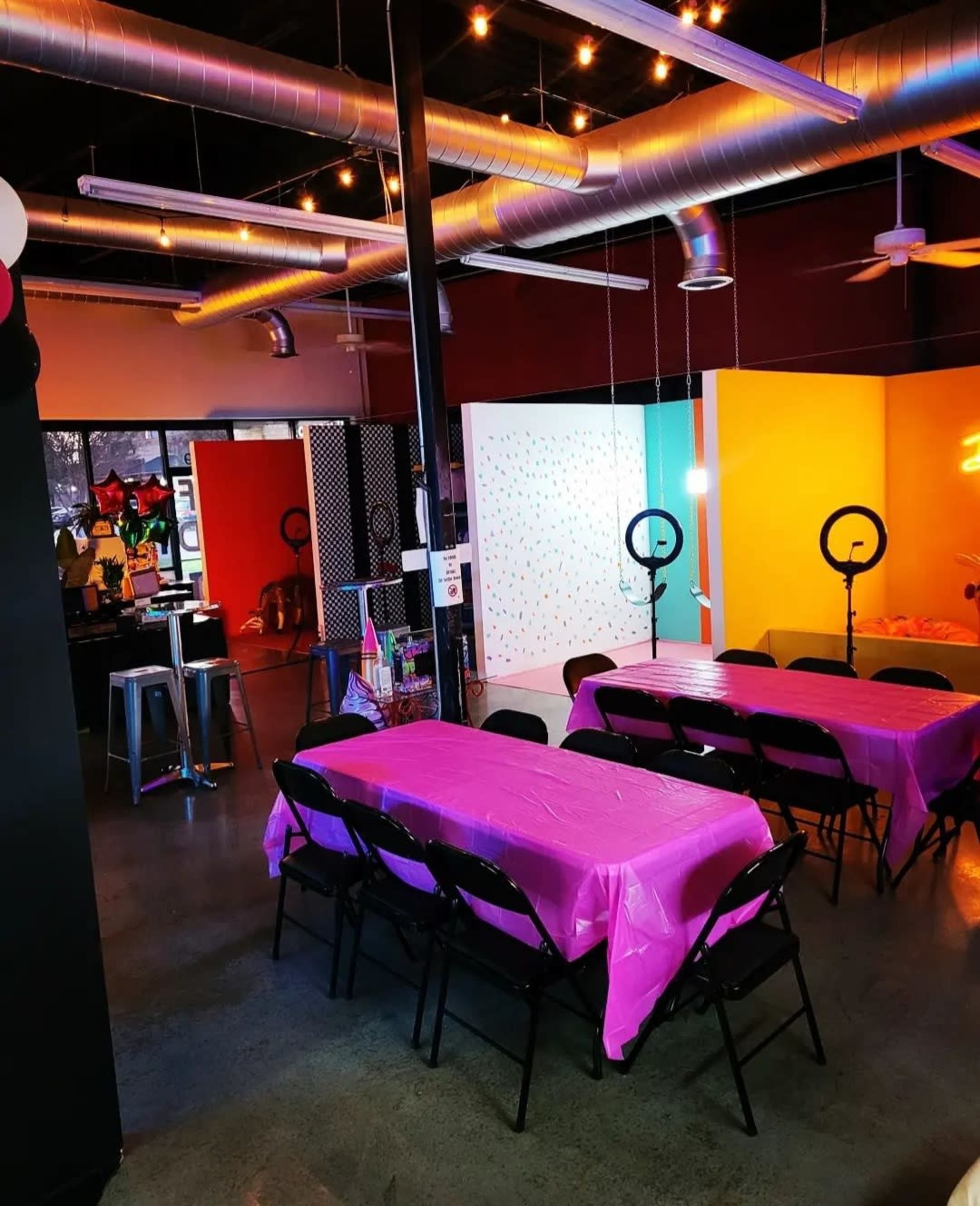 A party venue with several pink tables, bright colored walls, and ring lights set up.