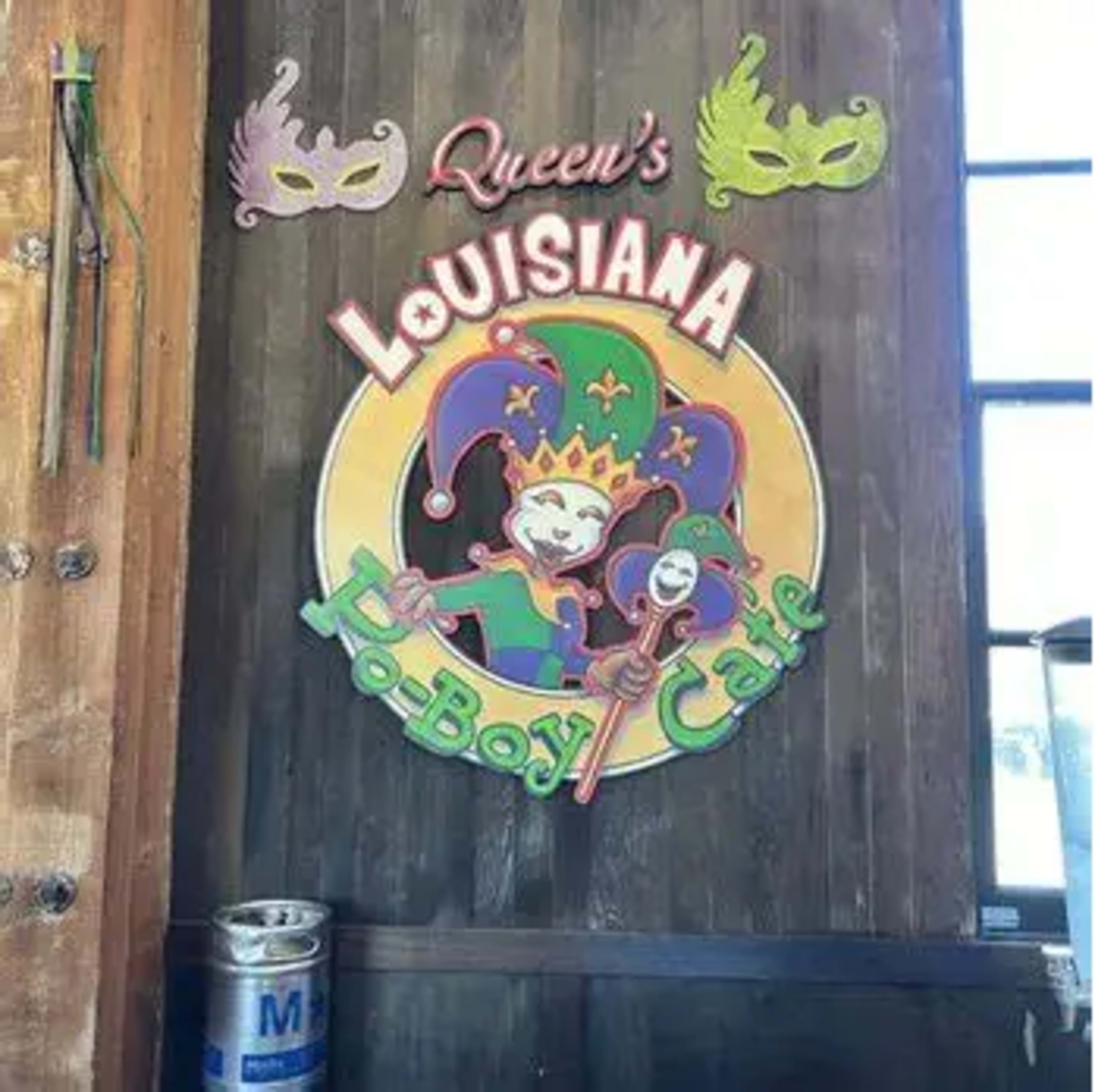 The image shows a colorful wooden sign for "Queen's Louisiana Po-Boy Cafe," featuring a jester and a festive design.