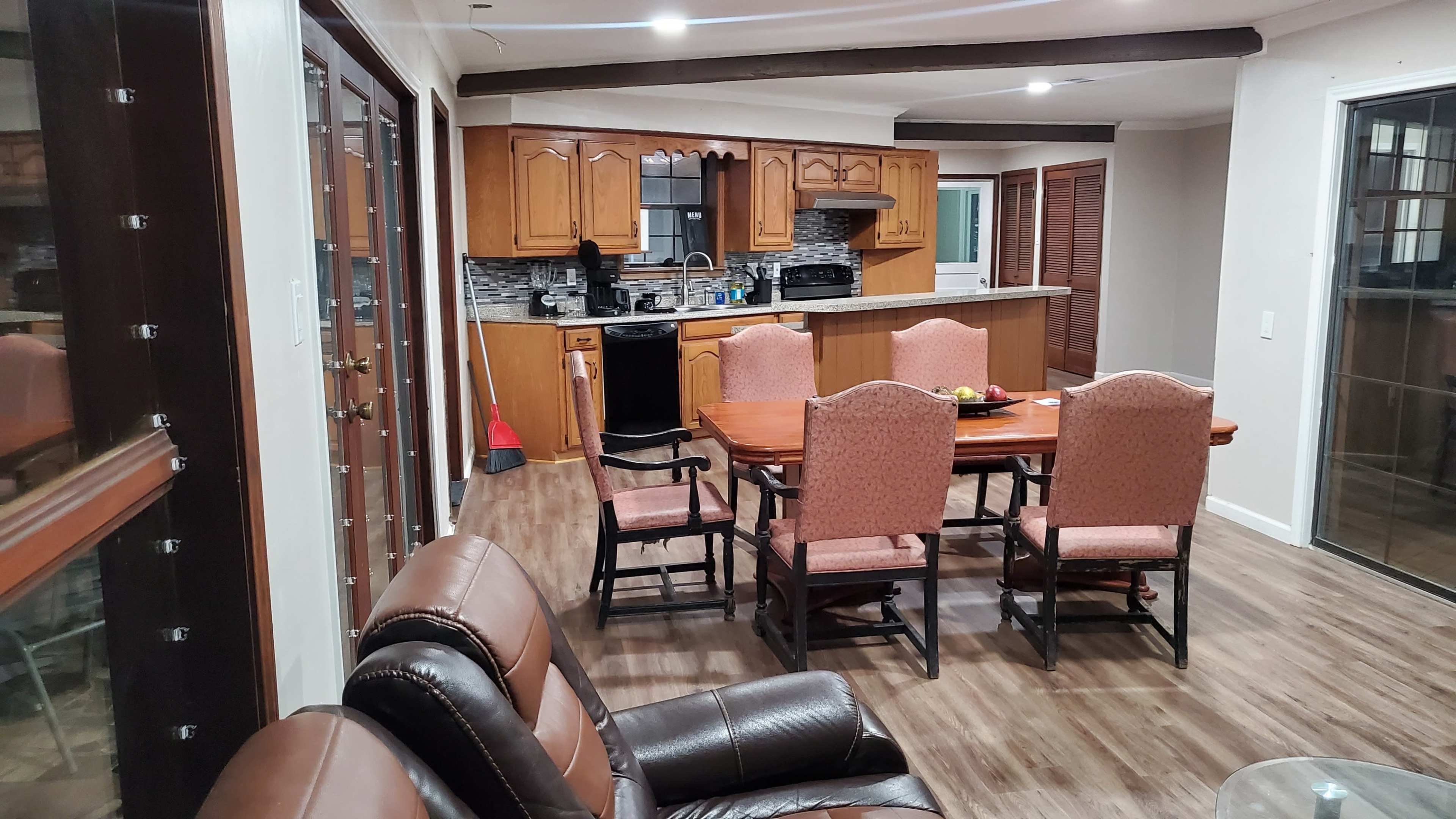 A dining area with a wooden table and chairs, leading into a kitchen with wooden cabinetry and appliances.