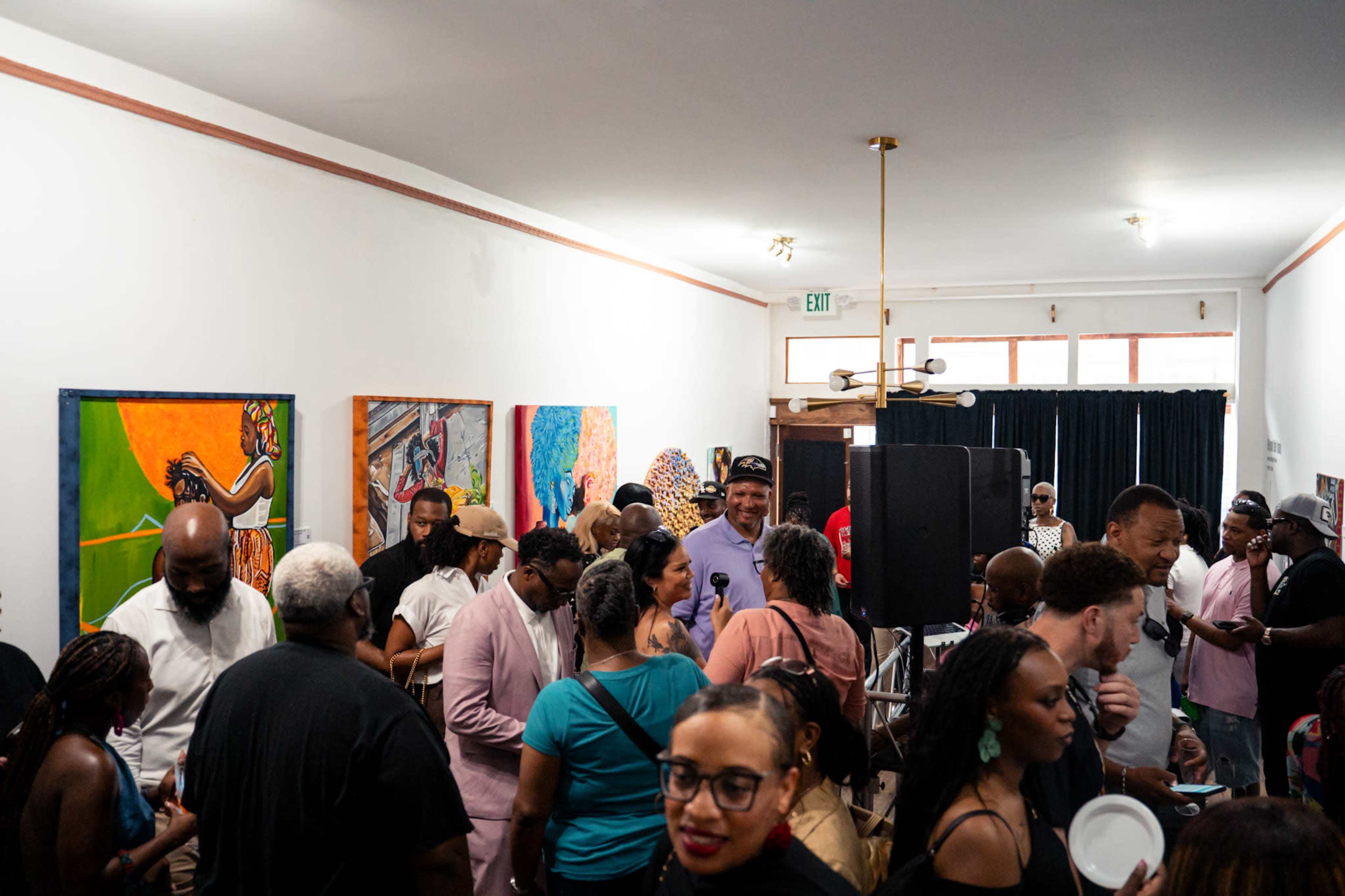A diverse group of people gathers in a room with colorful artwork on the walls, engaging in conversations and enjoying refreshments.