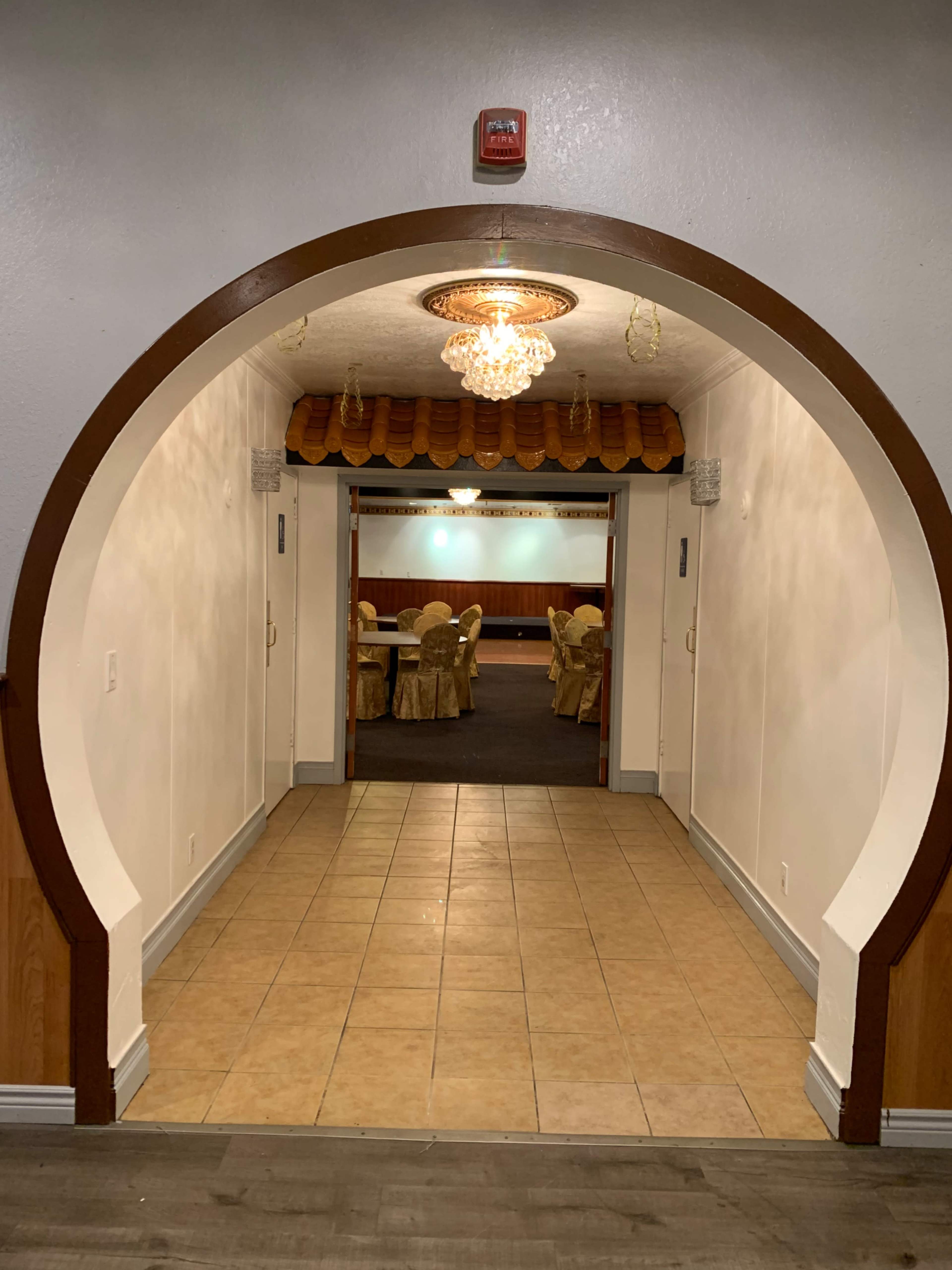 An arched entrance leads to a hallway with tiled flooring and a chandelier overhead, showcasing a seating area in the background.