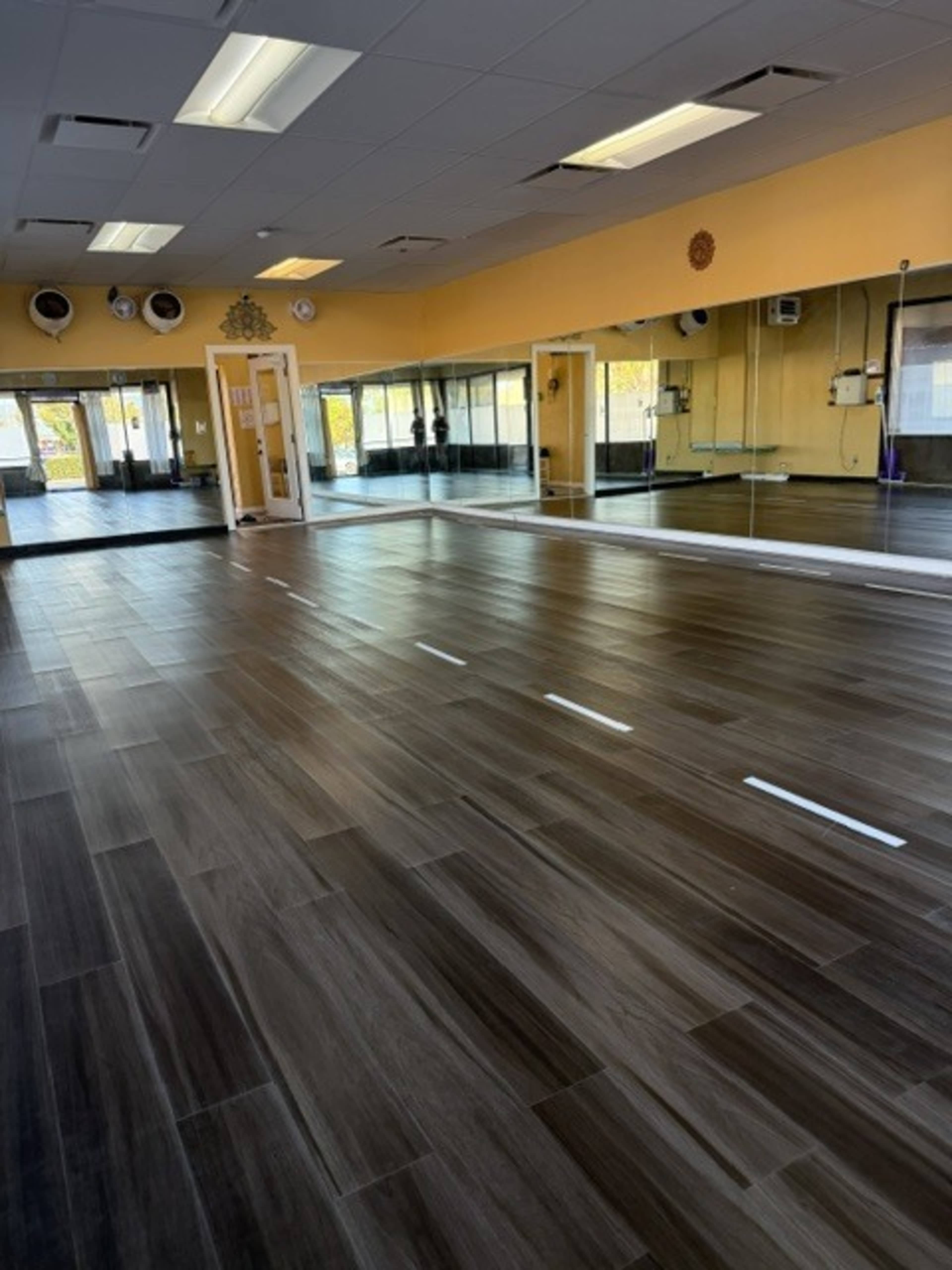 The image shows an empty studio space with large mirrors, wooden flooring, and yellow walls.