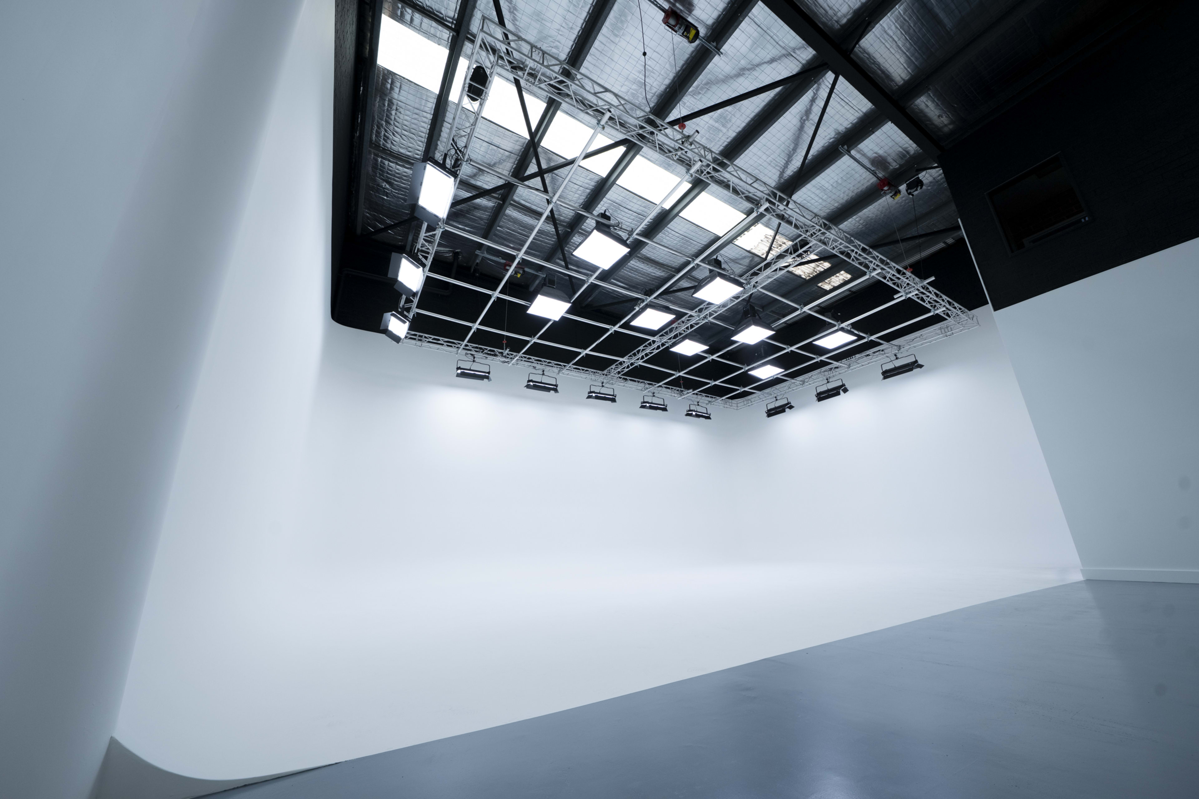 The image shows a spacious, empty photo studio with a white backdrop and overhead lights.