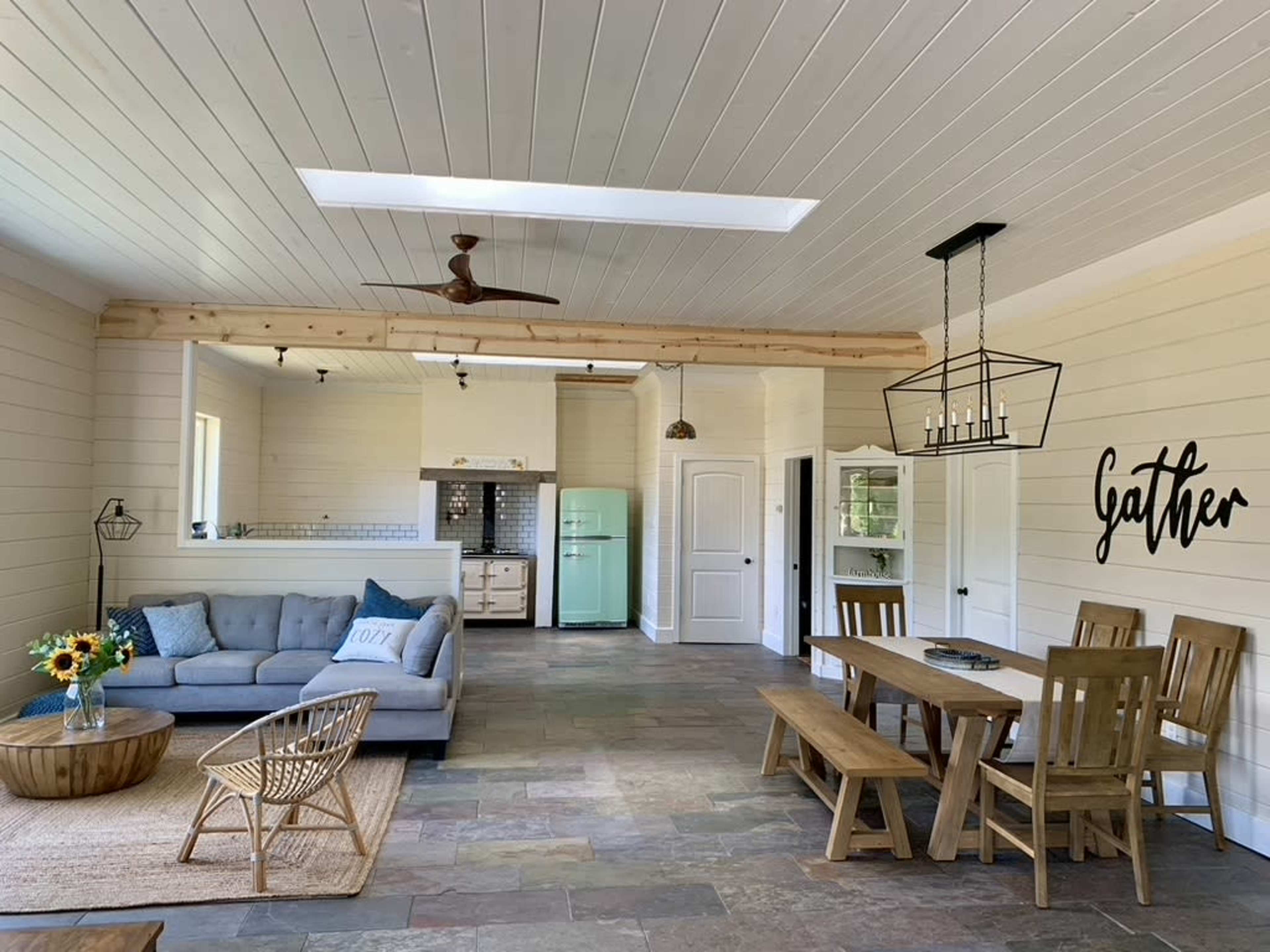 The image shows a spacious, modern living area with a sofa, dining table, and a kitchen featuring a vintage-style refrigerator.