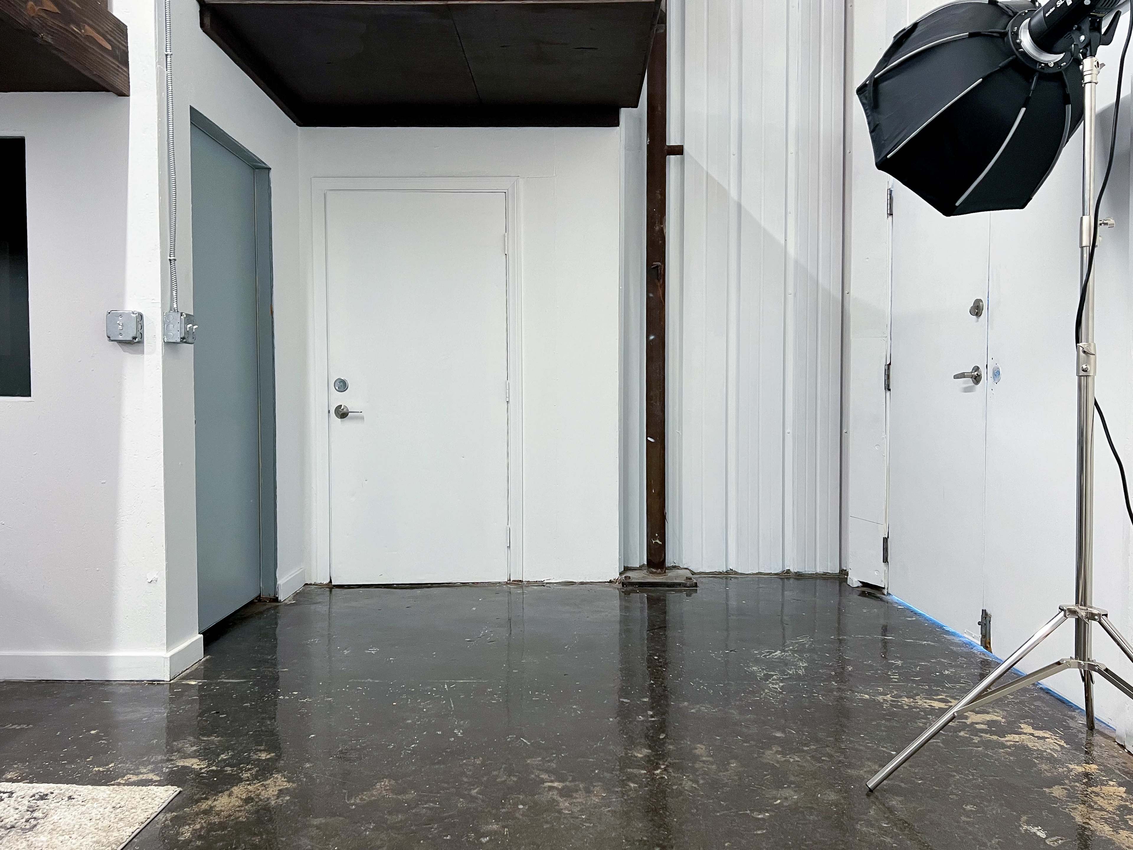 A minimalist interior space with two doors and a lighting setup on a stand.