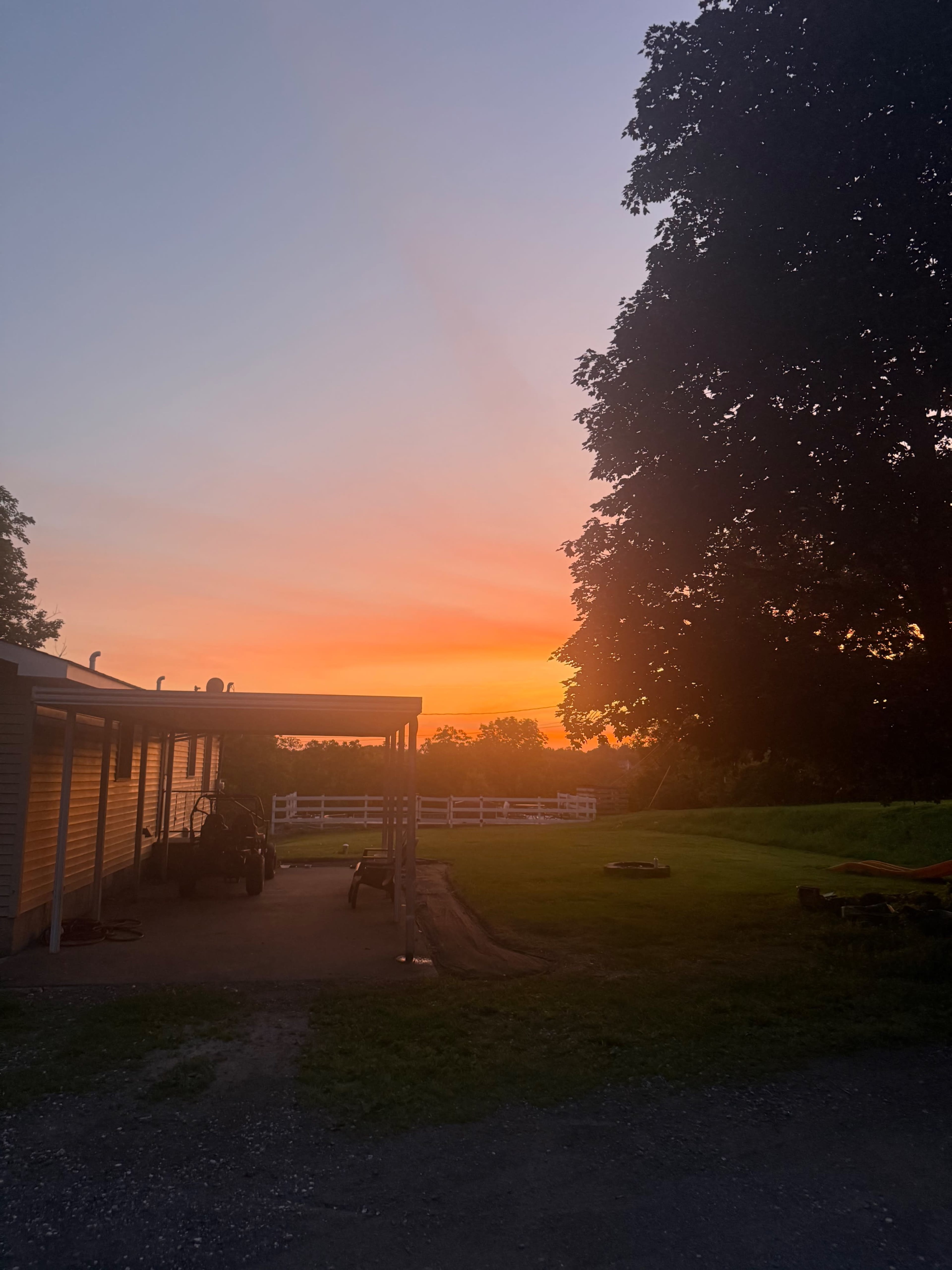 The image shows a sunset with vibrant colors behind a building, silhouetted by trees on the right side.