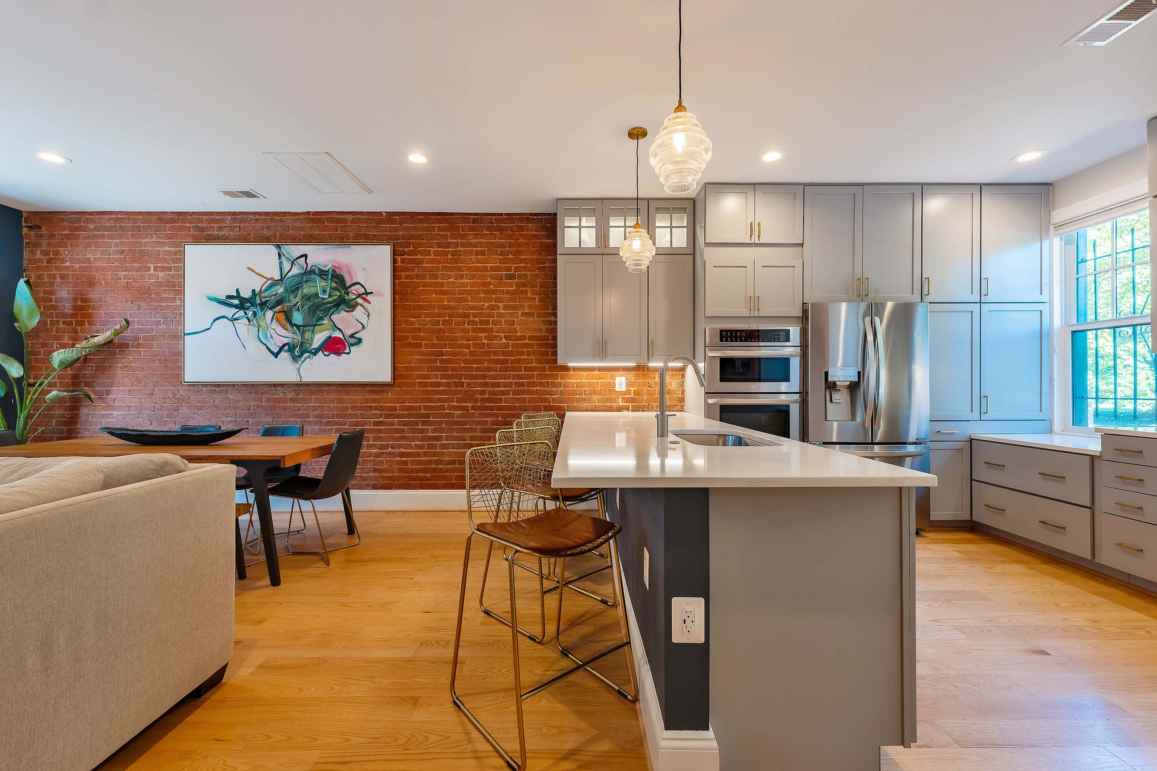A modern kitchen and dining area with a brick accent wall, sleek cabinetry, and a central island with bar stools.