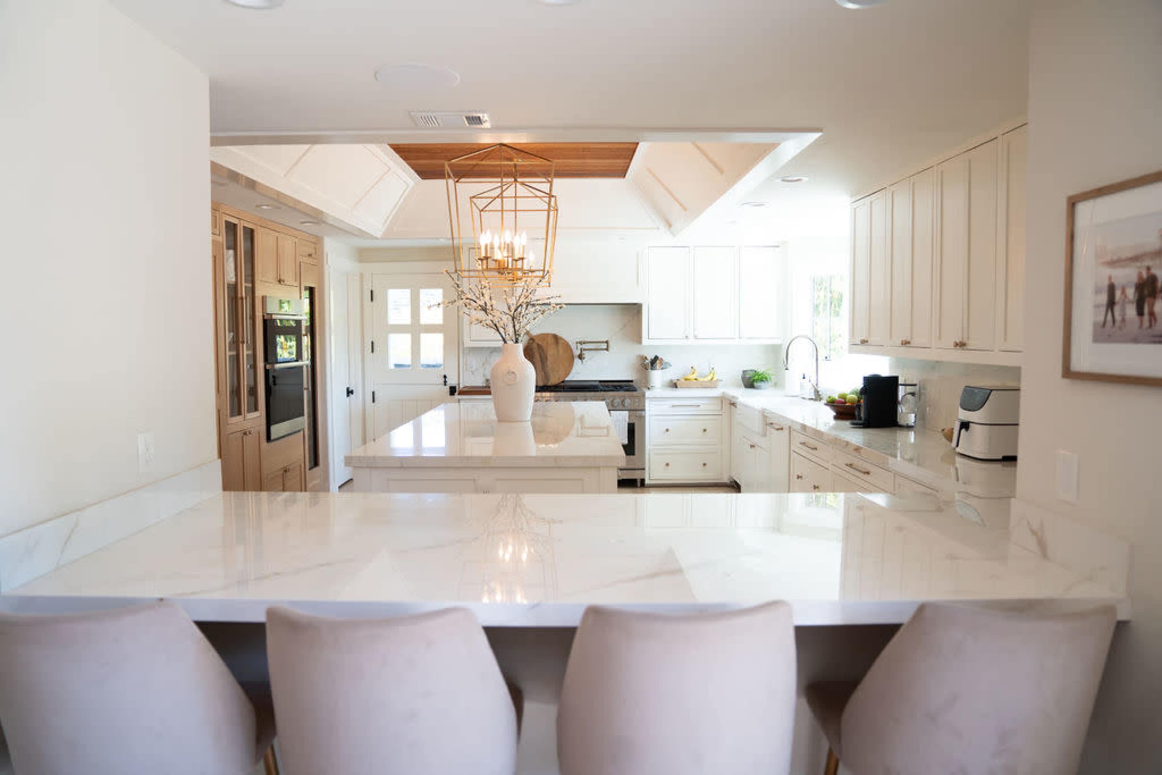 A modern kitchen features a marble countertop island with bar seating, white cabinetry, and stainless steel appliances.