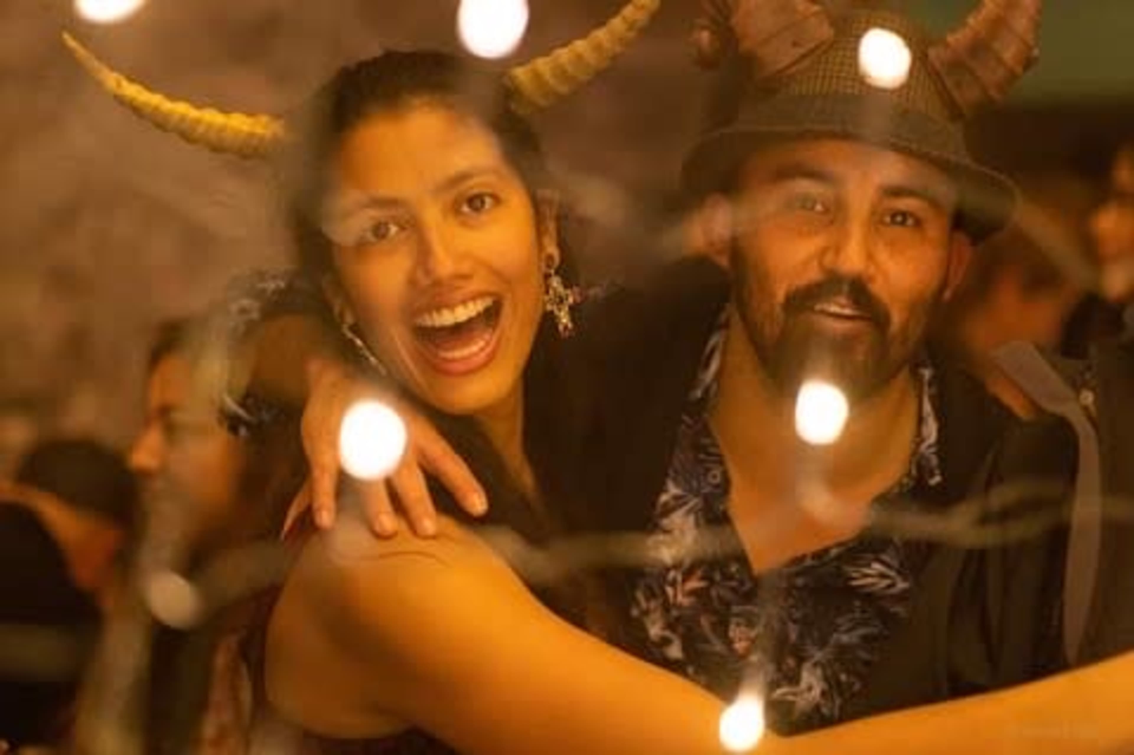 A woman with horned accessories and a man wearing a hat pose together in a warmly lit festive setting.