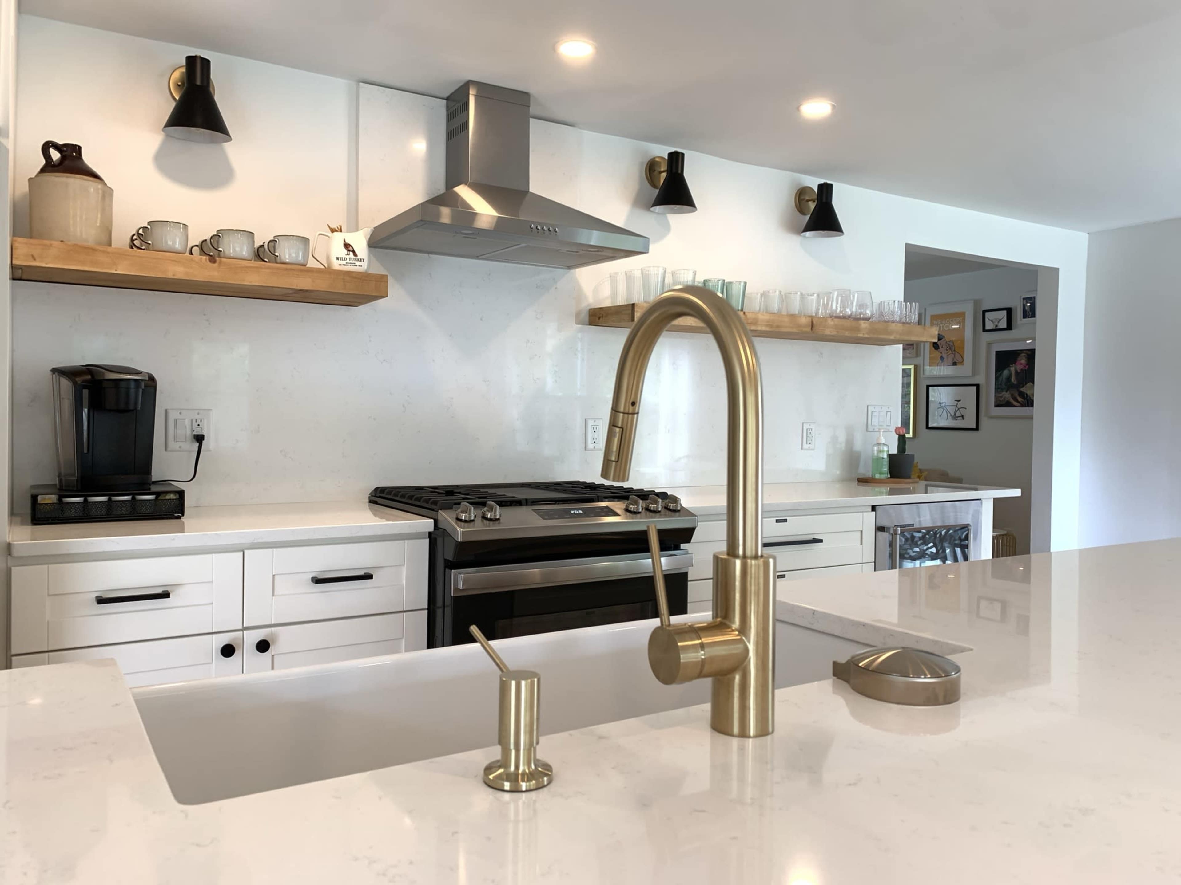 A modern kitchen with a stainless steel oven, a brass faucet, and open shelves displaying cups and glasses.