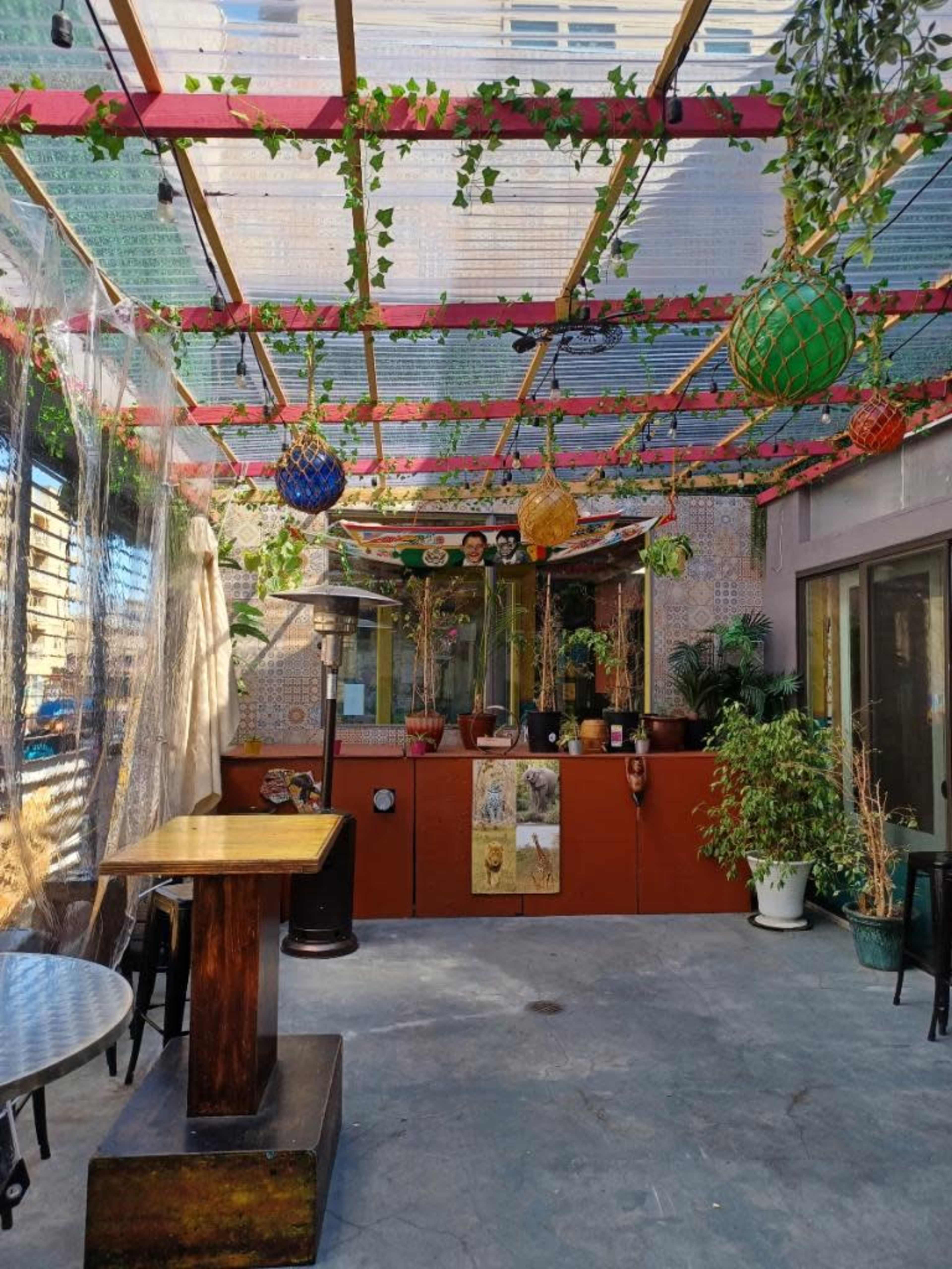 An outdoor dining area with a wooden table, potted plants, and colorful lanterns hanging from a canopy.