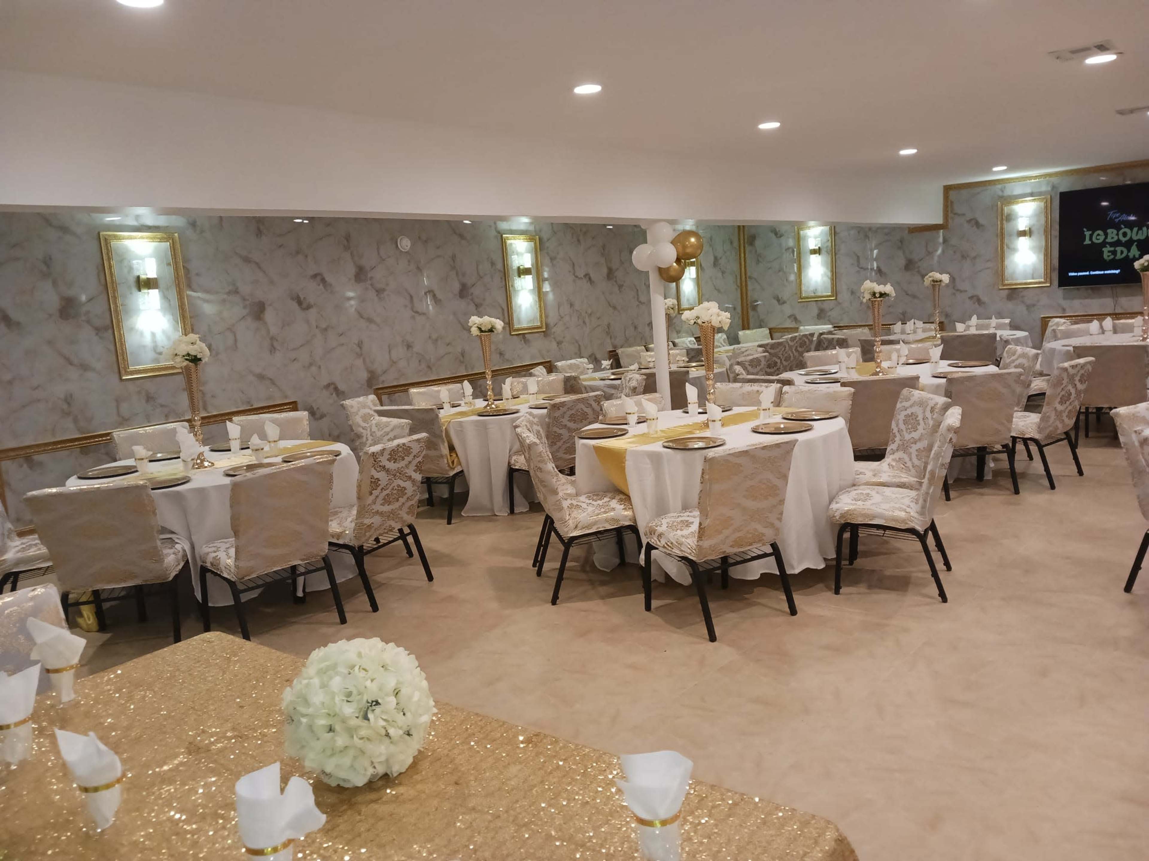 A banquet hall arranged with round tables covered in white and gold tablecloths, set for dining with floral centerpieces.