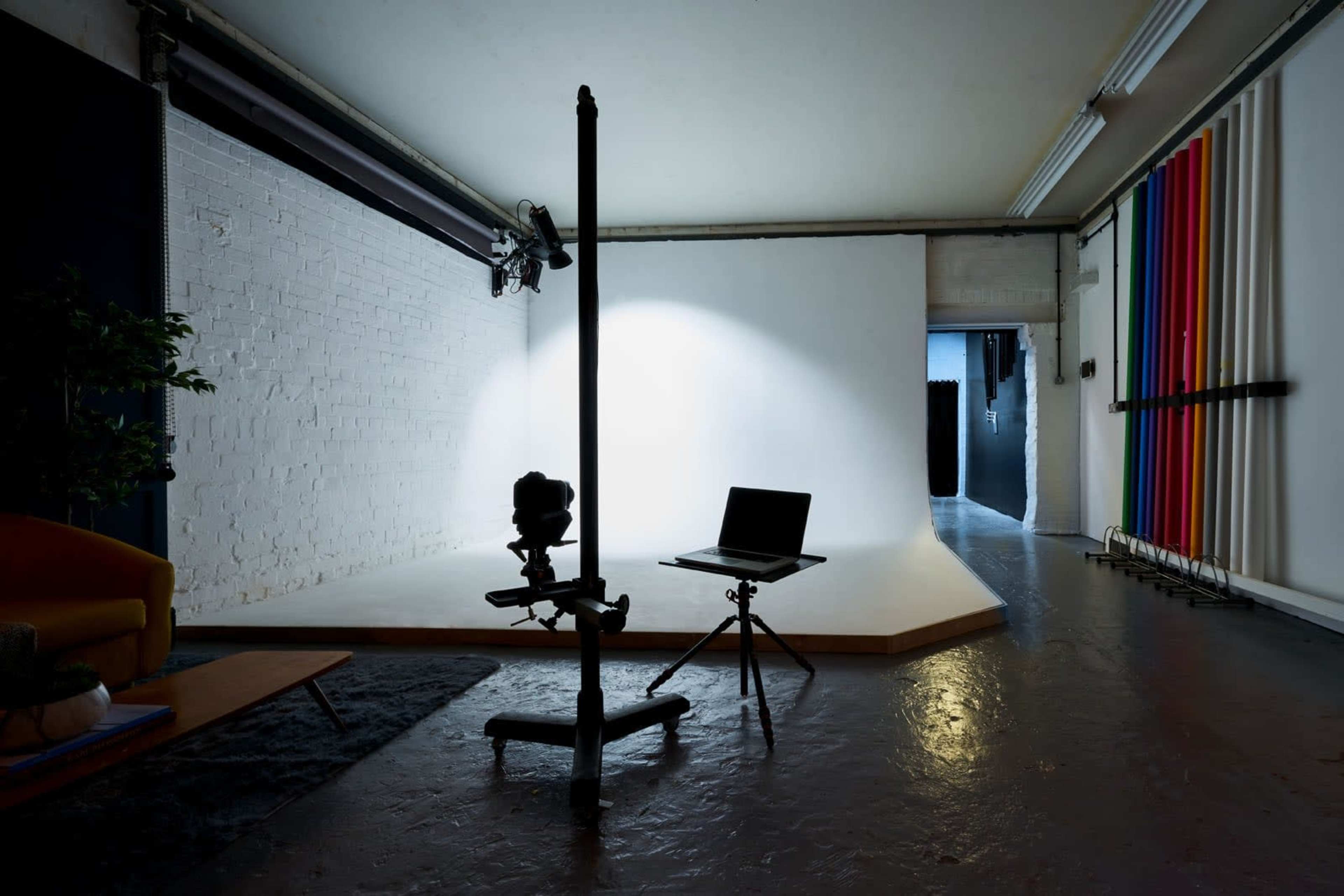 A photography studio with a lightstand, a laptop on a tripod, and a blank backdrop.