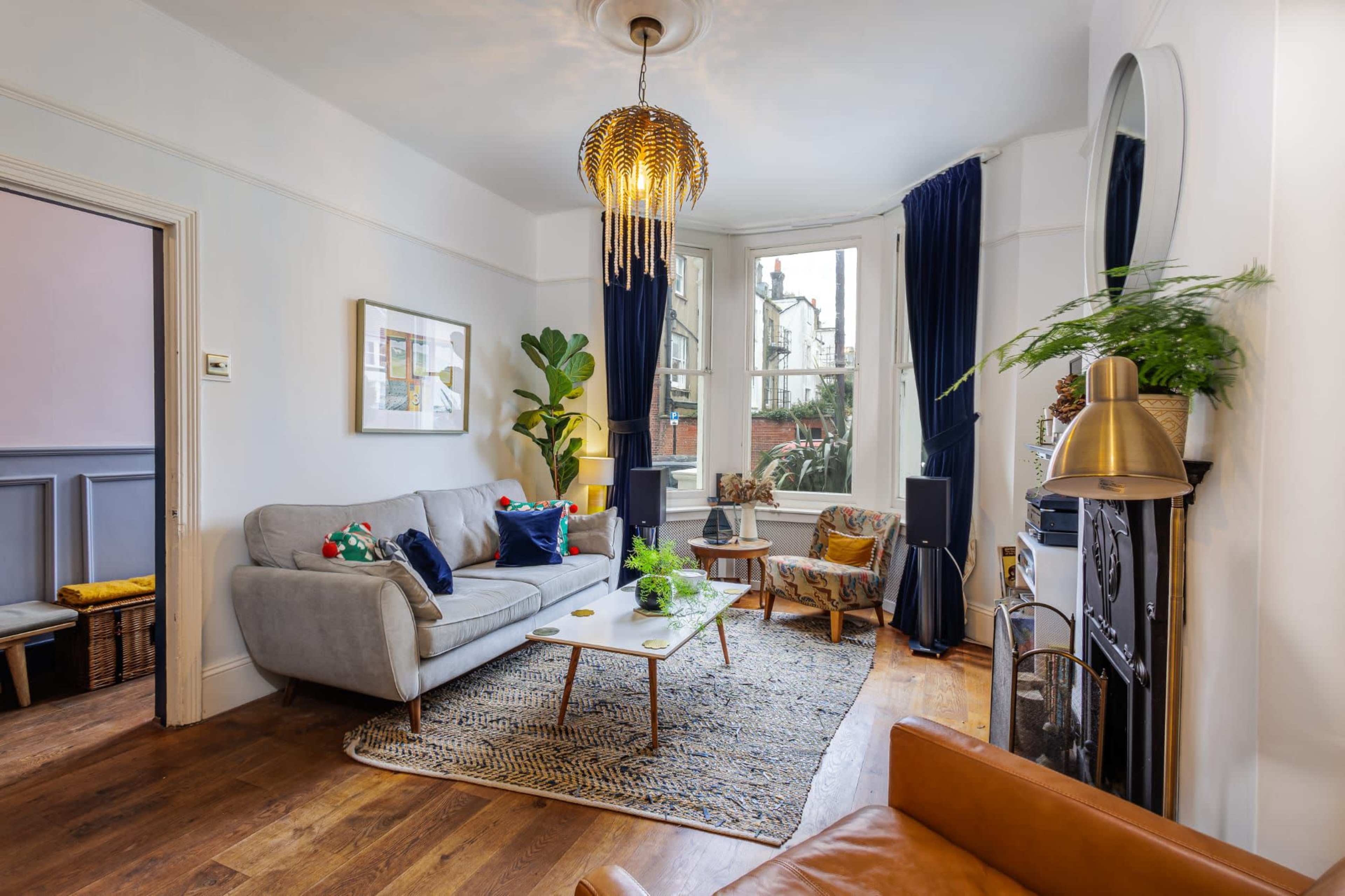 The image shows a well-decorated living room featuring a gray sofa, a wooden coffee table, and large windows with dark curtains.