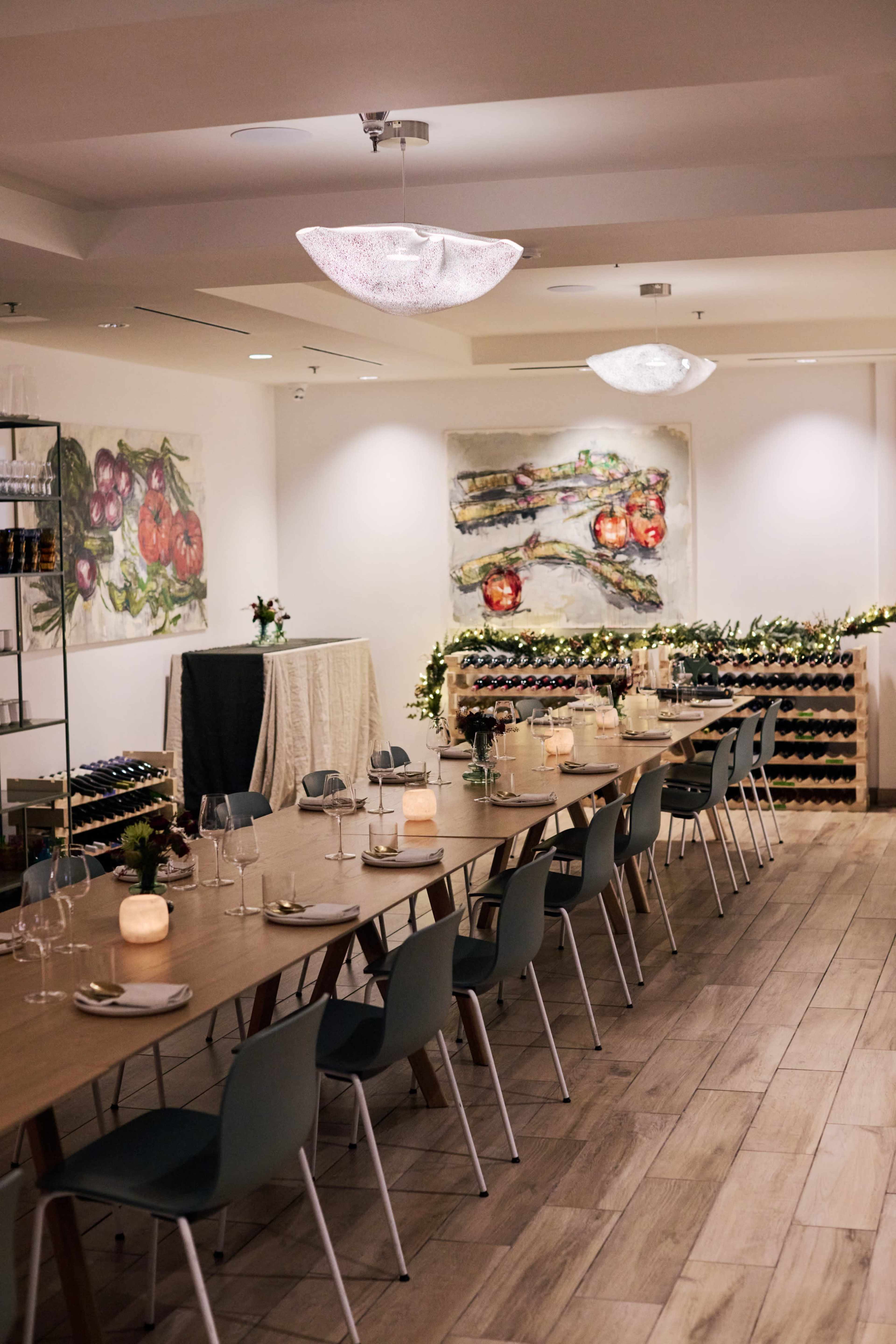 A modern restaurant interior features a long wooden dining table set with dishes and glassware, surrounded by elegant decorations and wine storage.