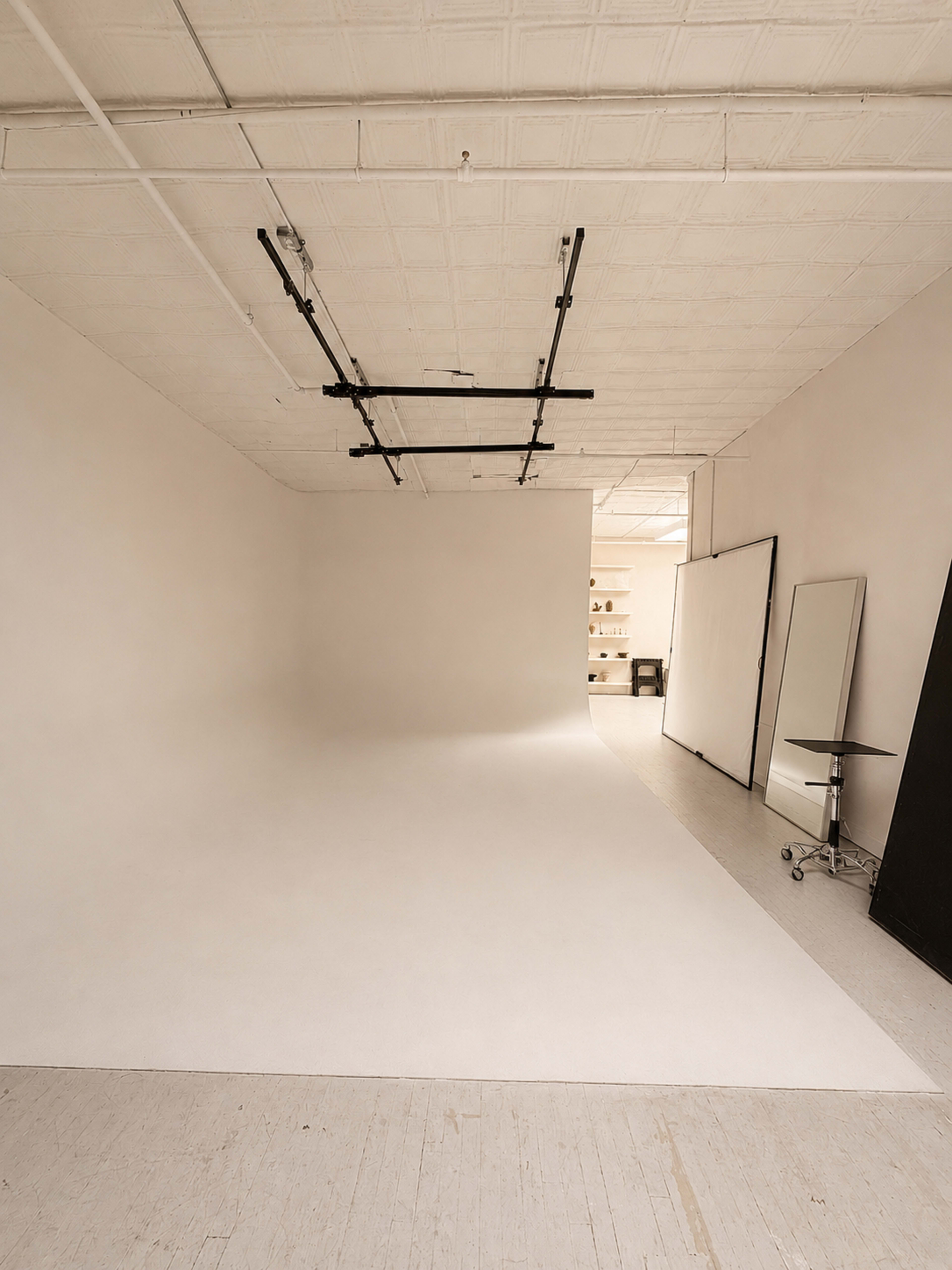 The image shows a minimalist studio space with a seamless backdrop, a mirror on wheels, and a black panel on one side.