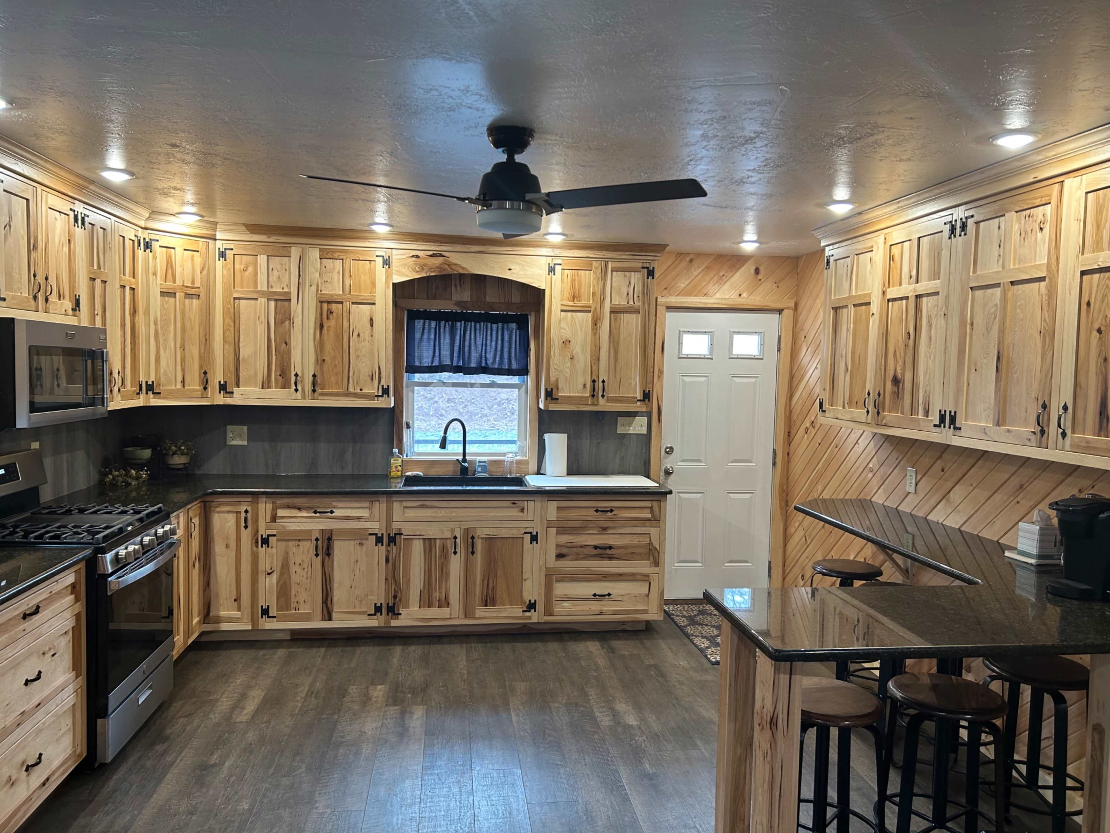 The kitchen features wooden cabinets, a ceiling fan, a stainless steel stove, and a small bar area with stools.