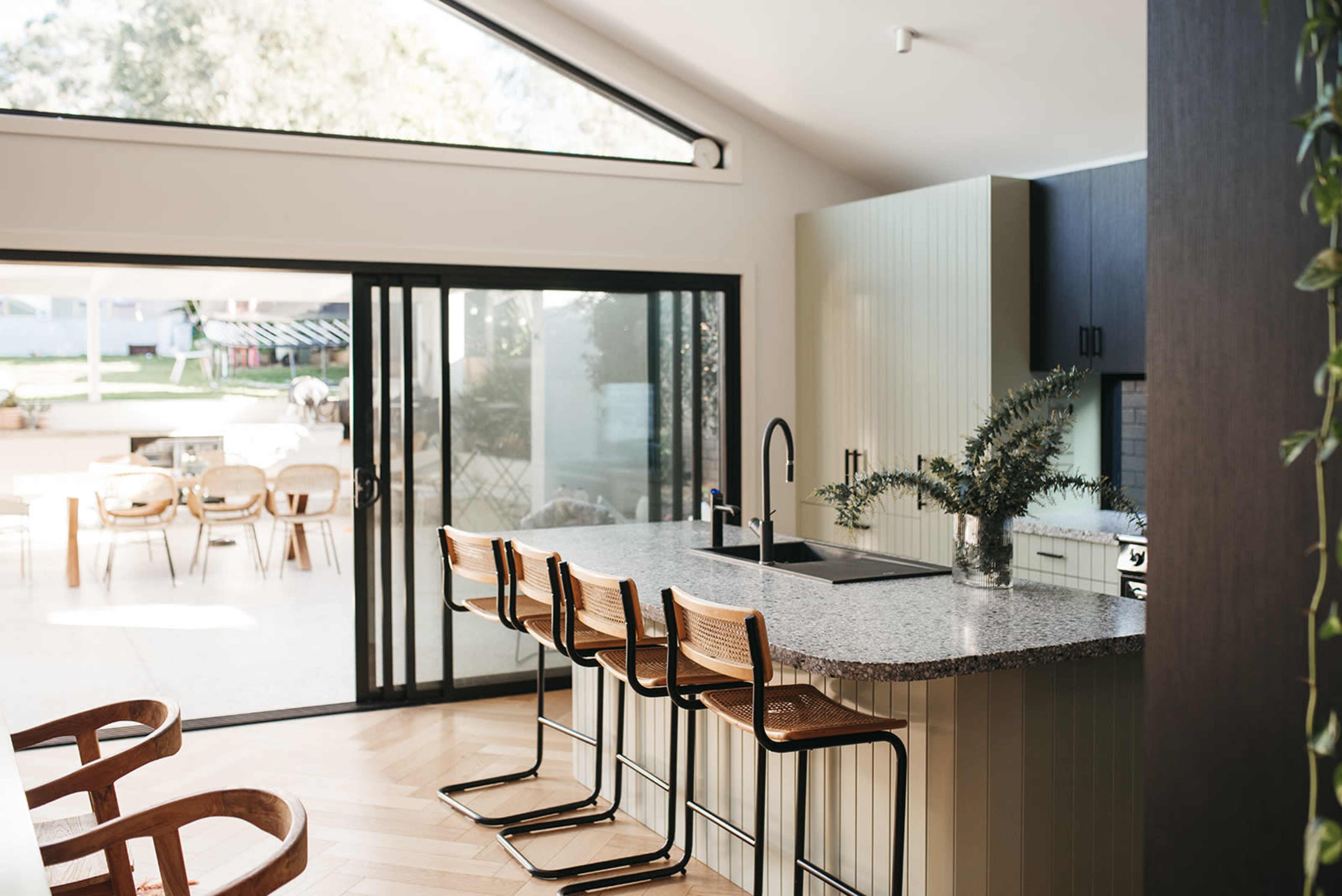 A modern kitchen features a multipurpose island with seating and large glass doors opening to an outdoor patio area.