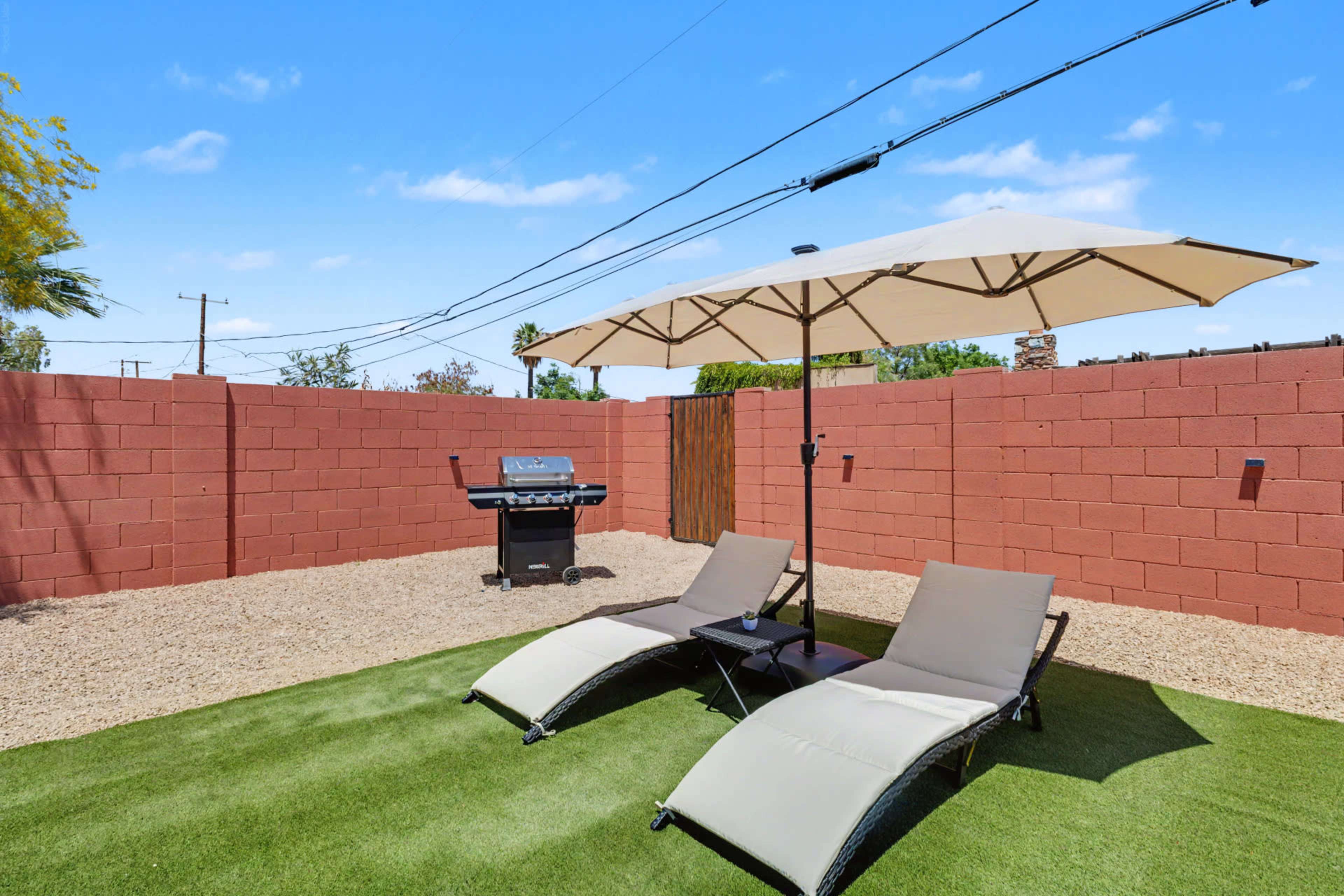 The image depicts a backyard area with two lounge chairs under an umbrella, a grill in the background, and gravel landscaping.