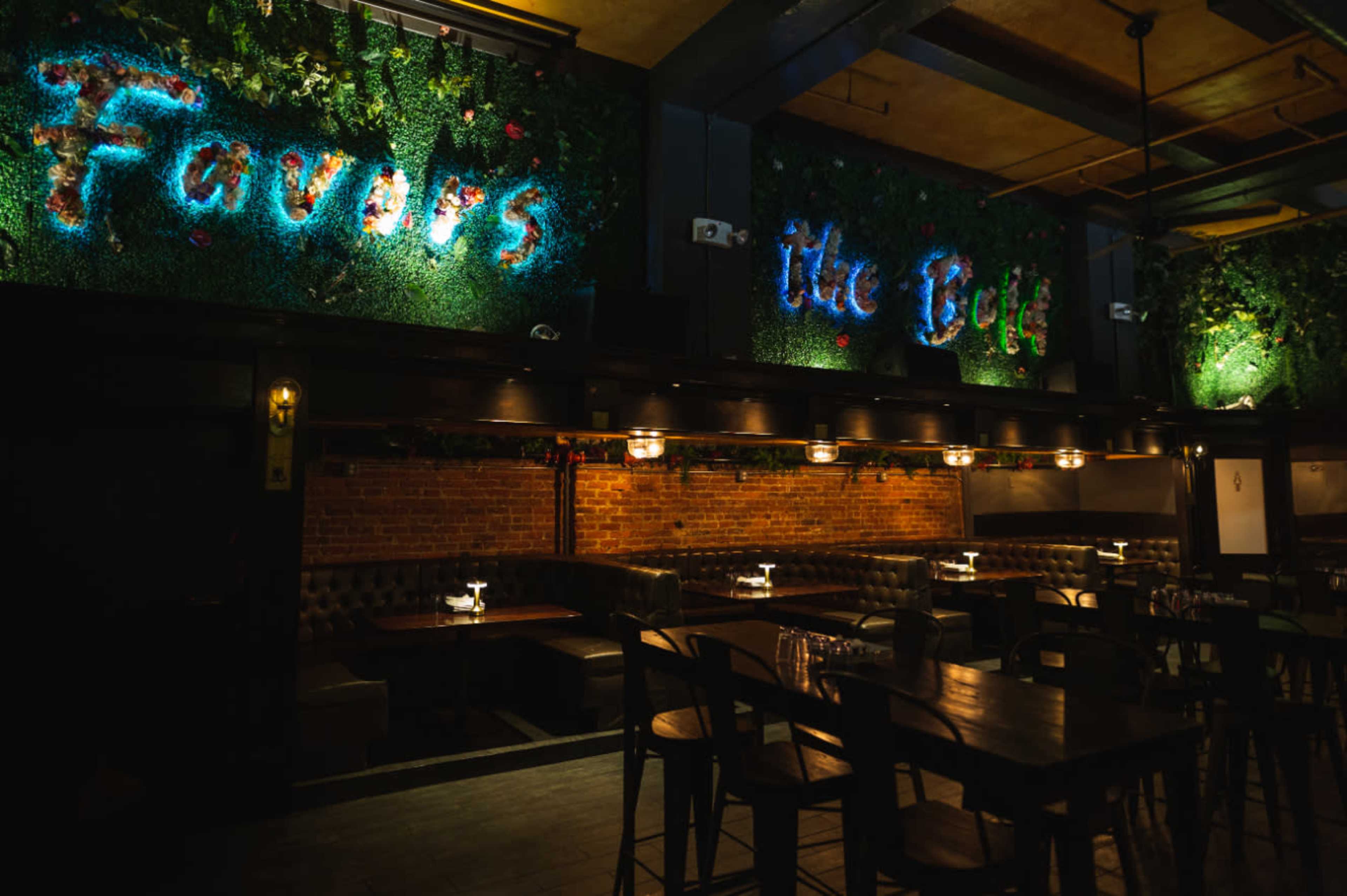 The image depicts a dimly lit restaurant interior with green walls featuring illuminated text that reads "Favors the Bold," alongside dark wooden tables and chairs arranged in a cozy layout.