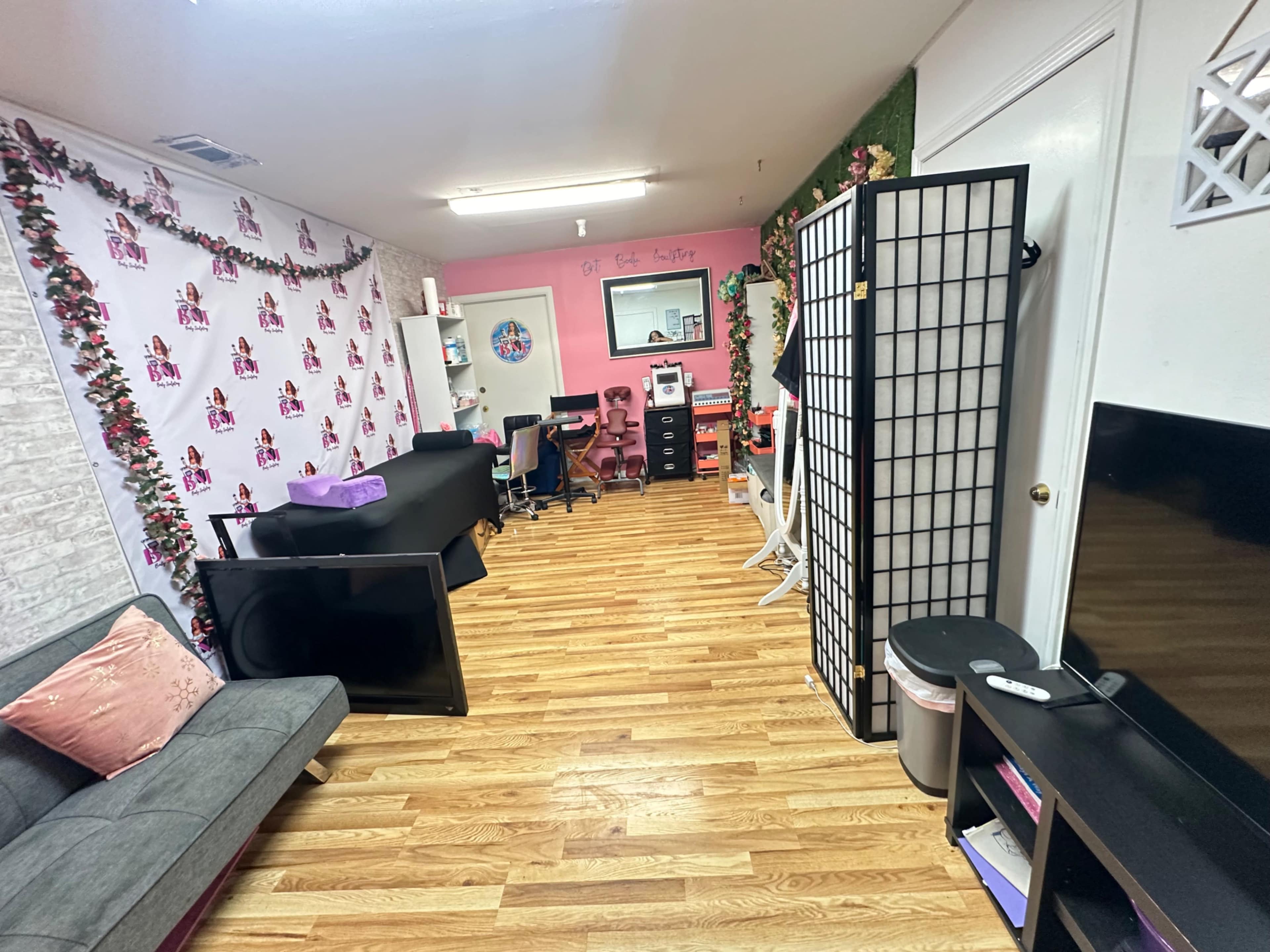 The image shows a brightly decorated office space with wood flooring, featuring a couch, a reception area, and decorative elements on the walls.