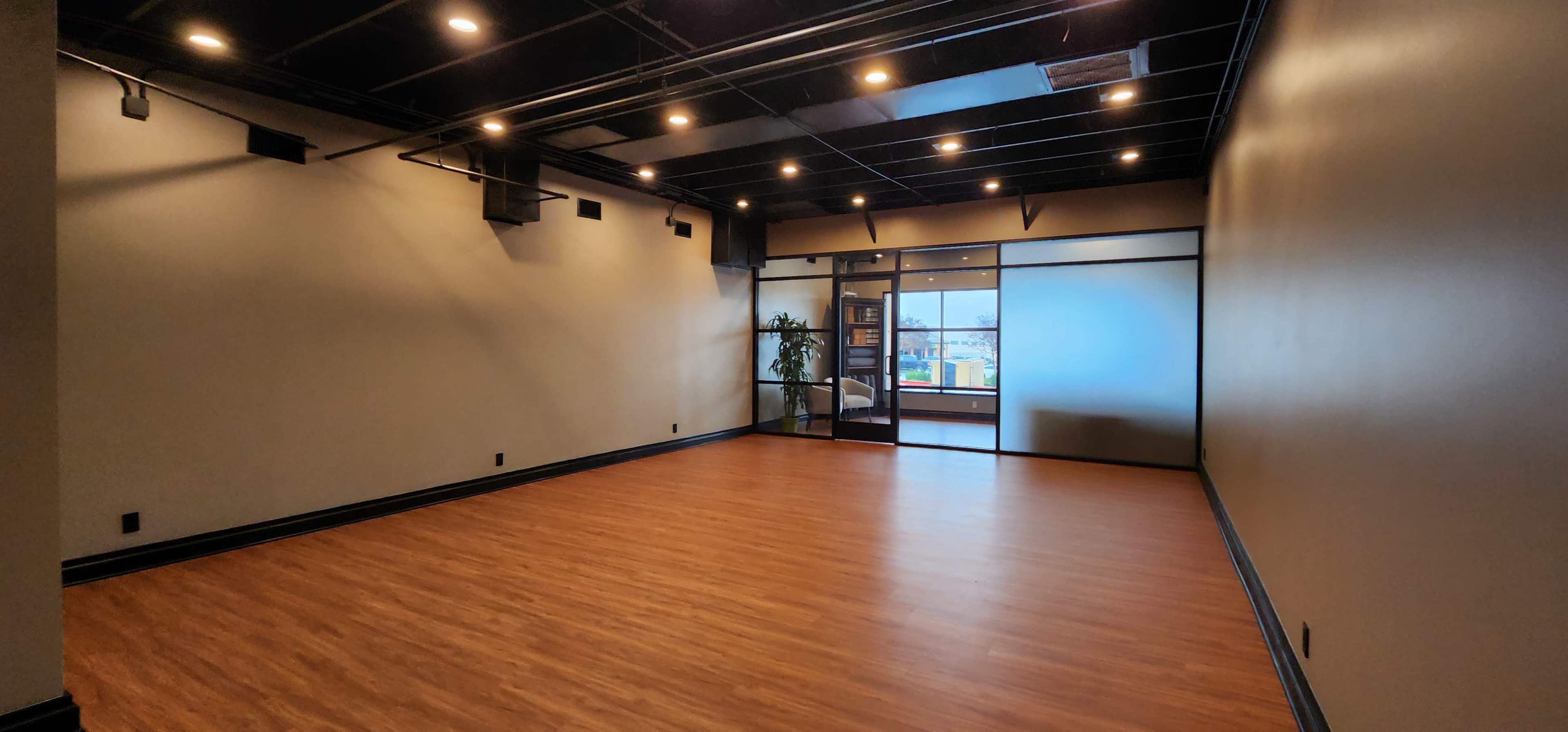 An empty room with wooden flooring, modern lighting, and a glass door leading to an exterior view.