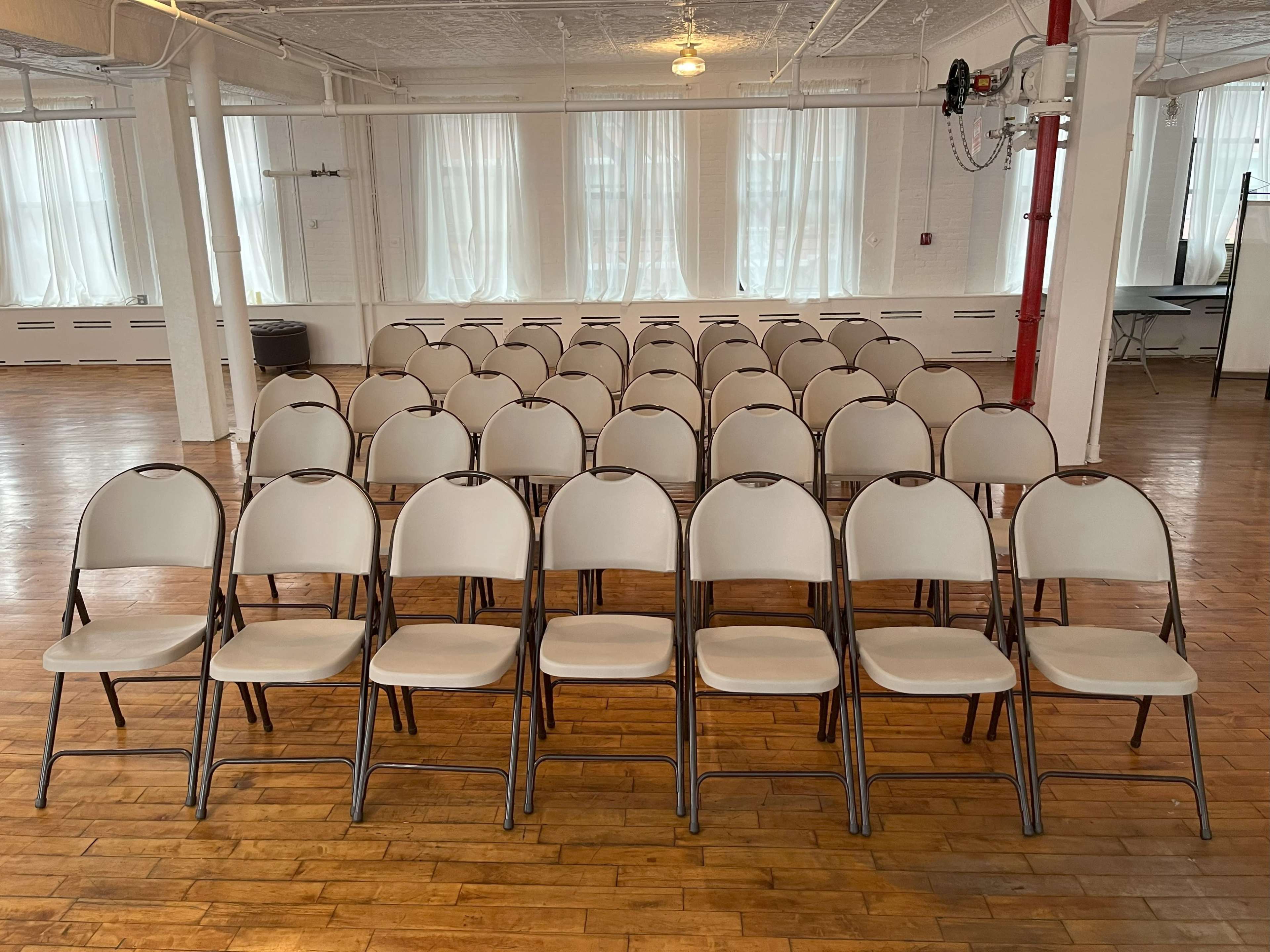 A row of empty folding chairs is arranged in a well-lit room with large windows.