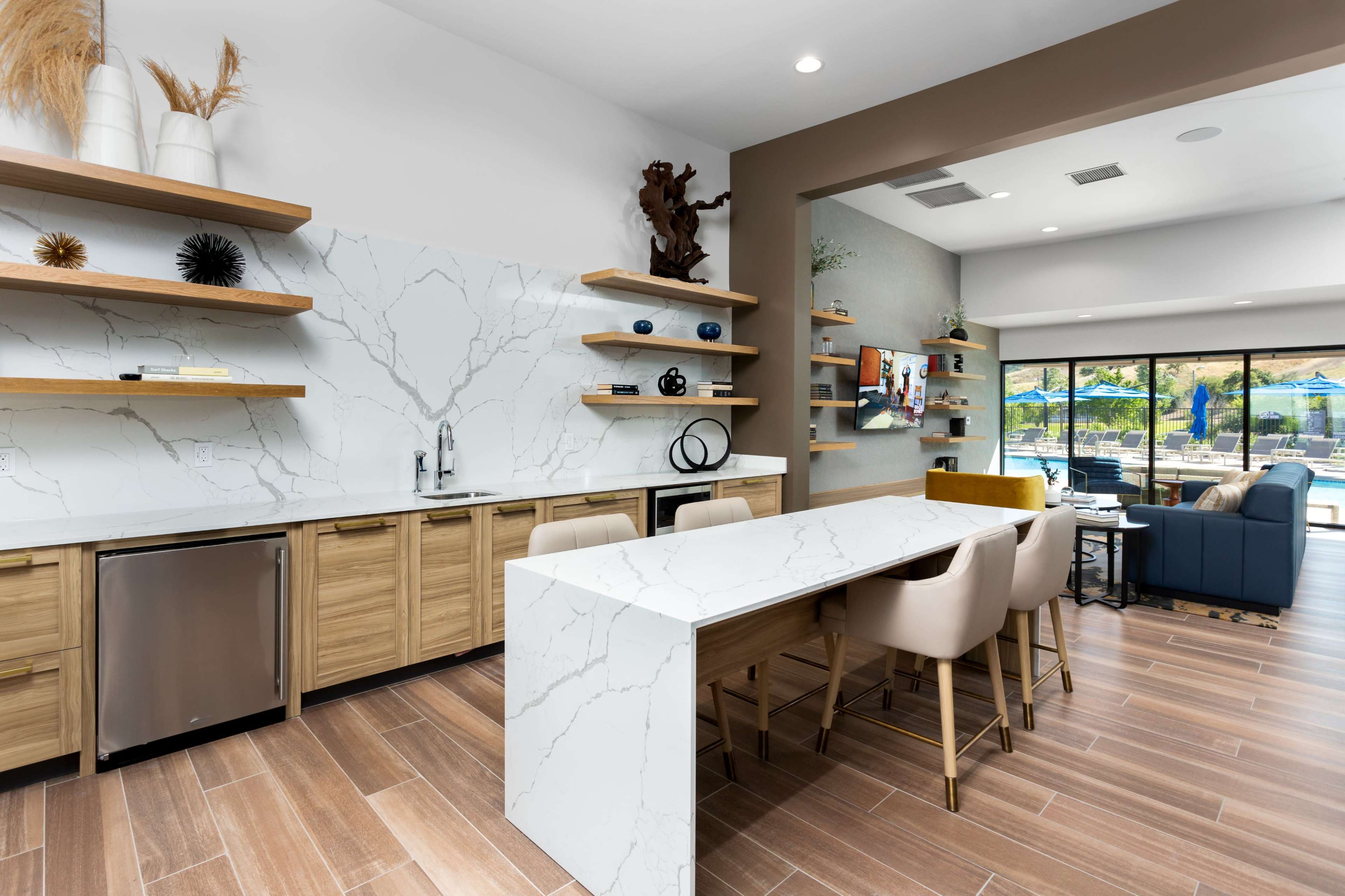A modern kitchen with a large white marble countertop, wooden cabinets, and open shelving displaying decorative items.