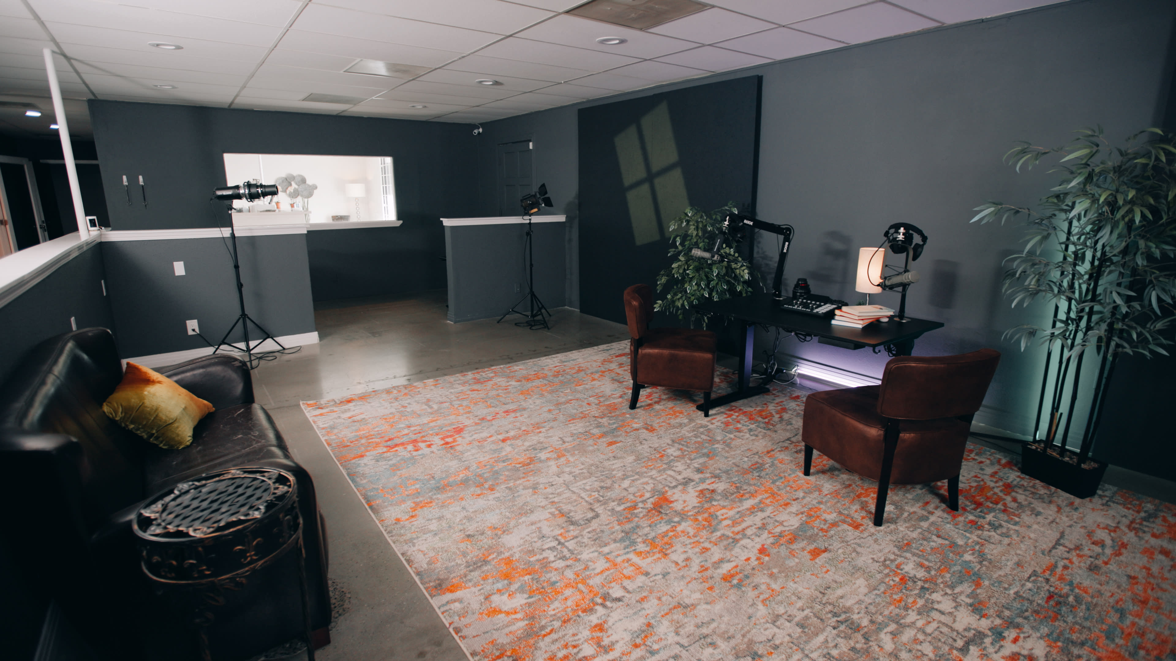 A modern office space featuring two brown chairs, a desk with a lamp, and a large area rug, all set against gray walls and minimalistic decor.