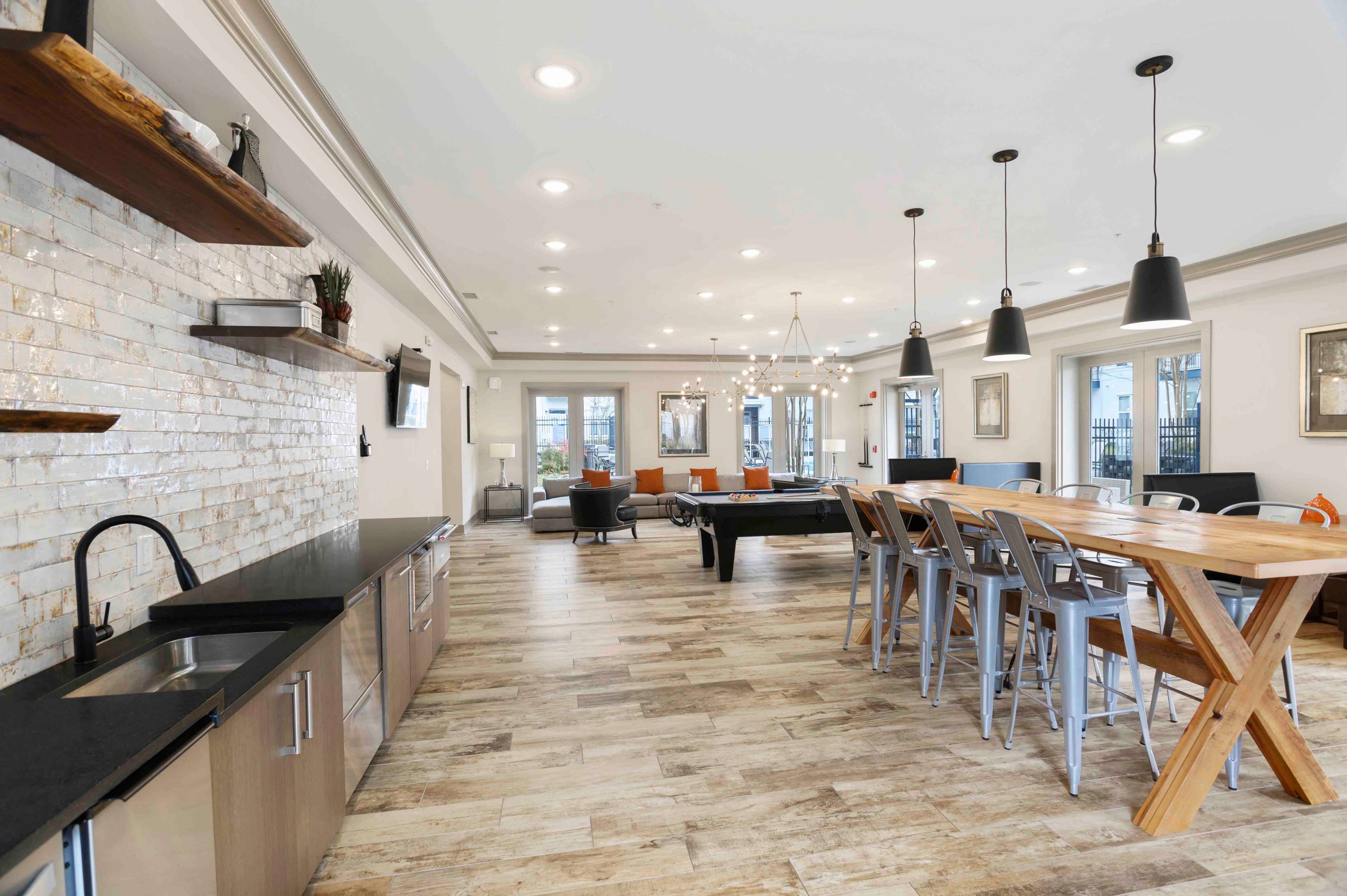 A modern communal space with a kitchen area, a dining table made of wood, a pool table, and seating arranged in a well-lit room.