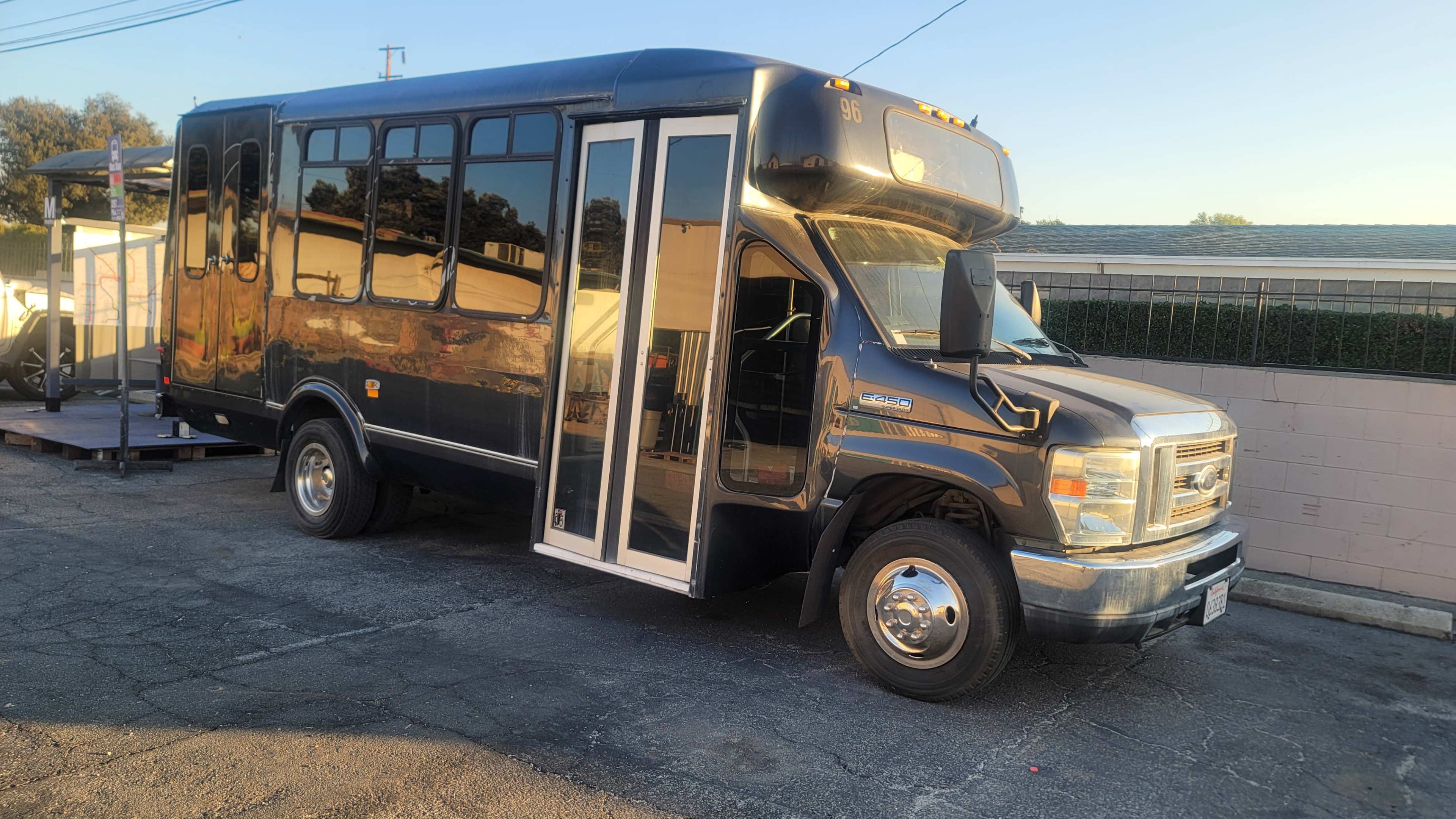 A black shuttle bus with an open door is parked on a paved lot in front of a building.