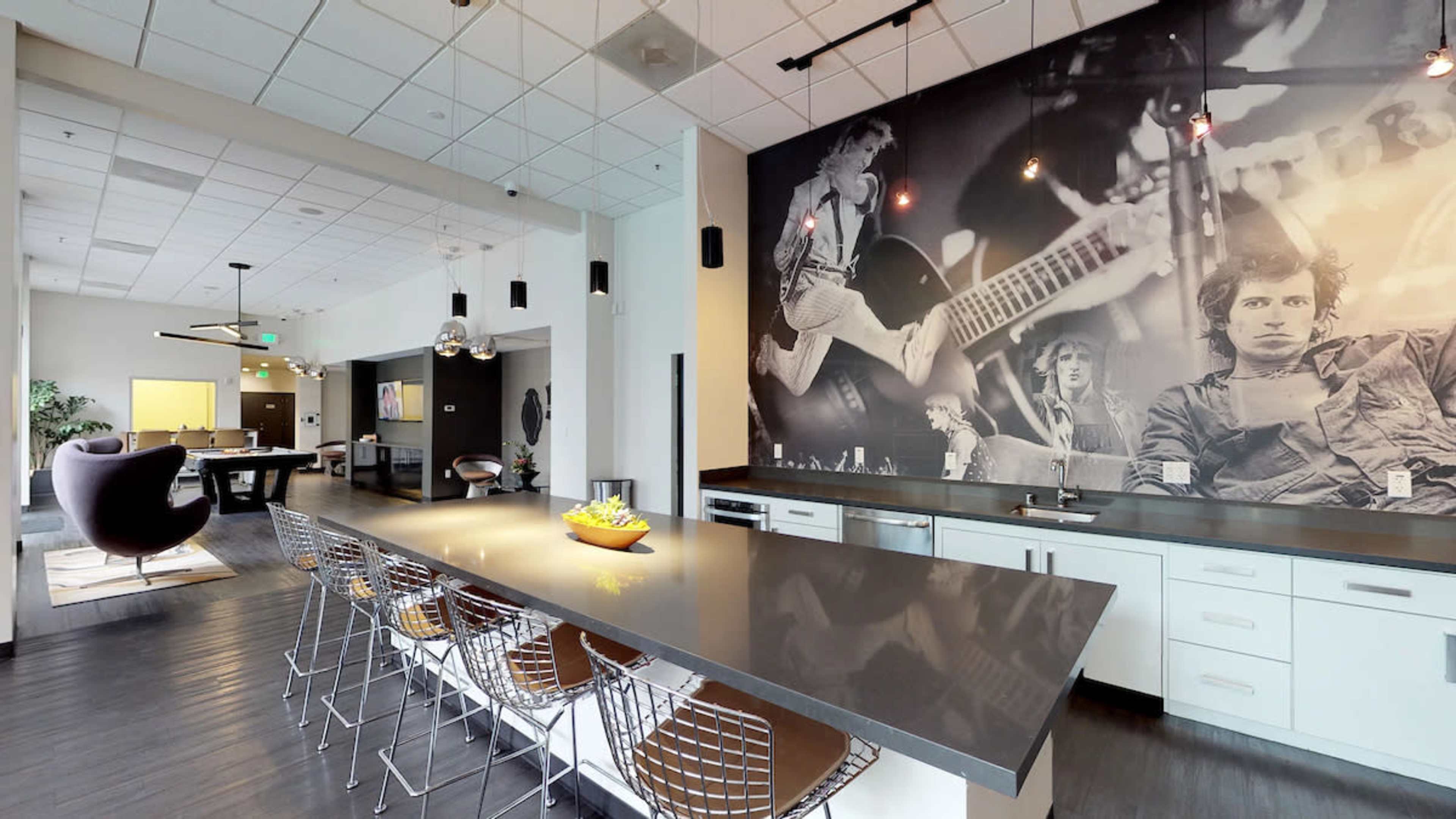 A modern kitchen features a long countertop with bar stools and a large wall mural of musicians.