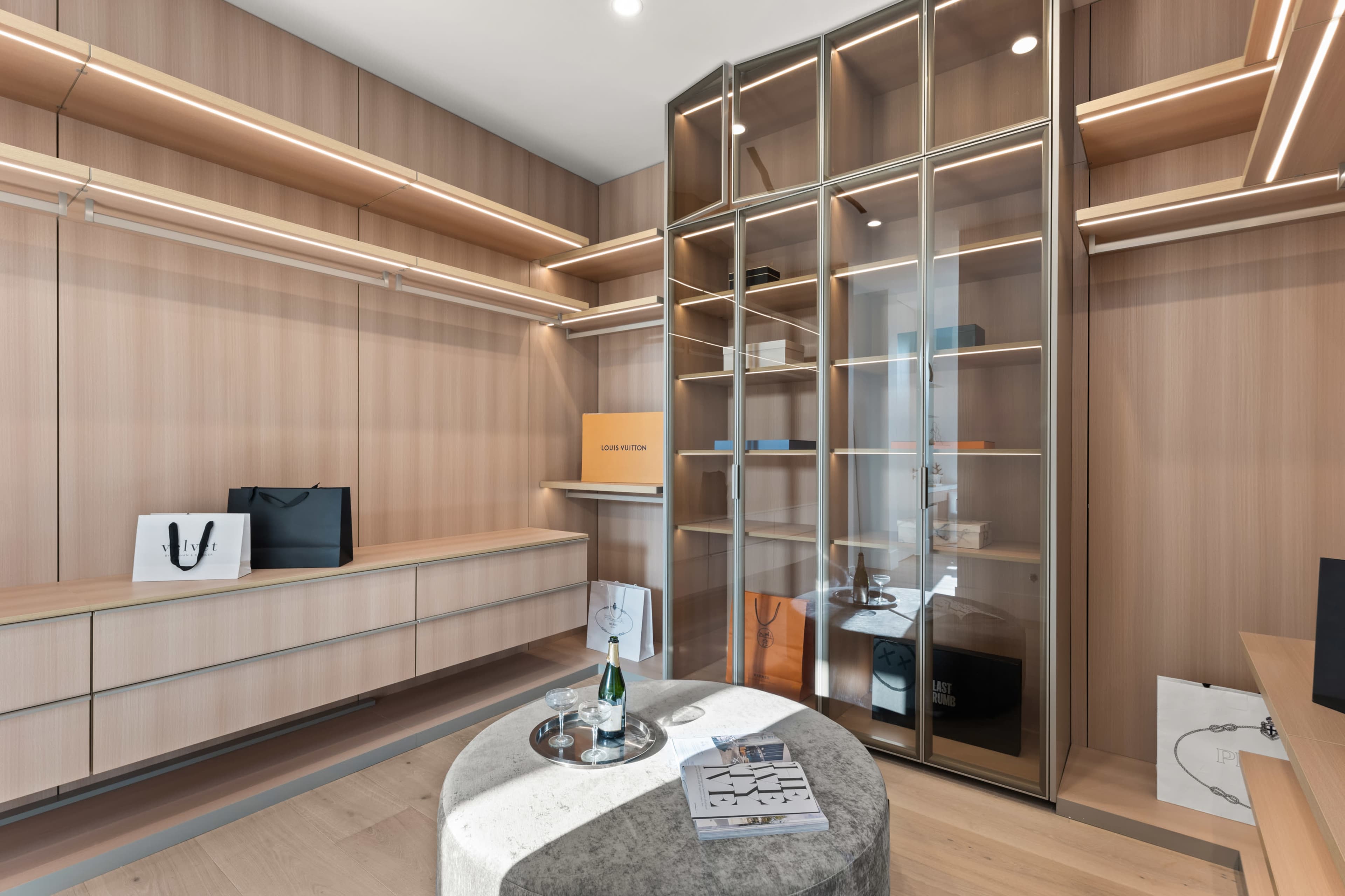 A modern, organized walk-in closet featuring built-in shelves, a glass display case, and a central stone coffee table.