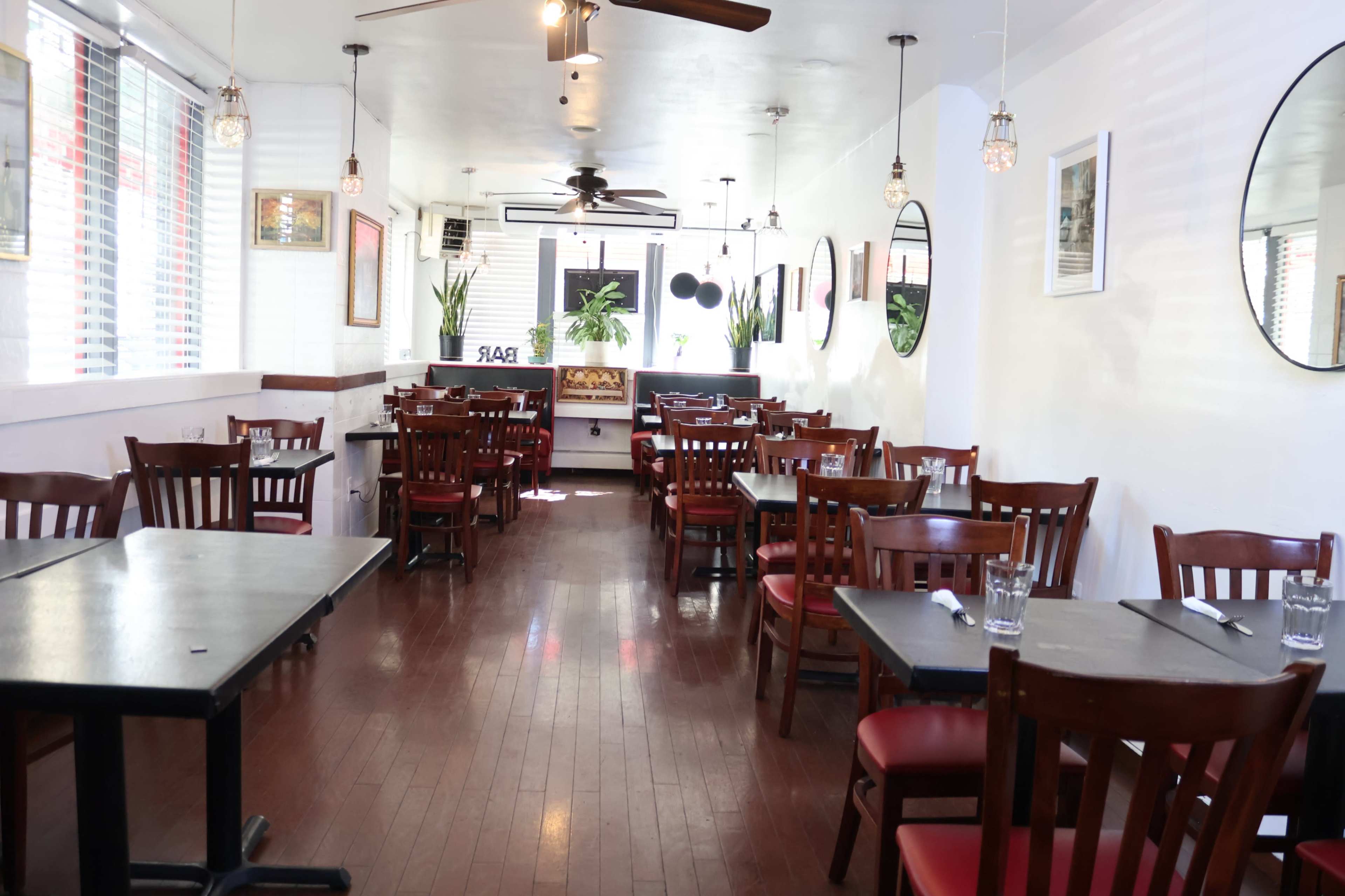 The image depicts a restaurant interior with wooden tables and chairs arranged in a spacious layout, featuring large windows that allow natural light to fill the room.