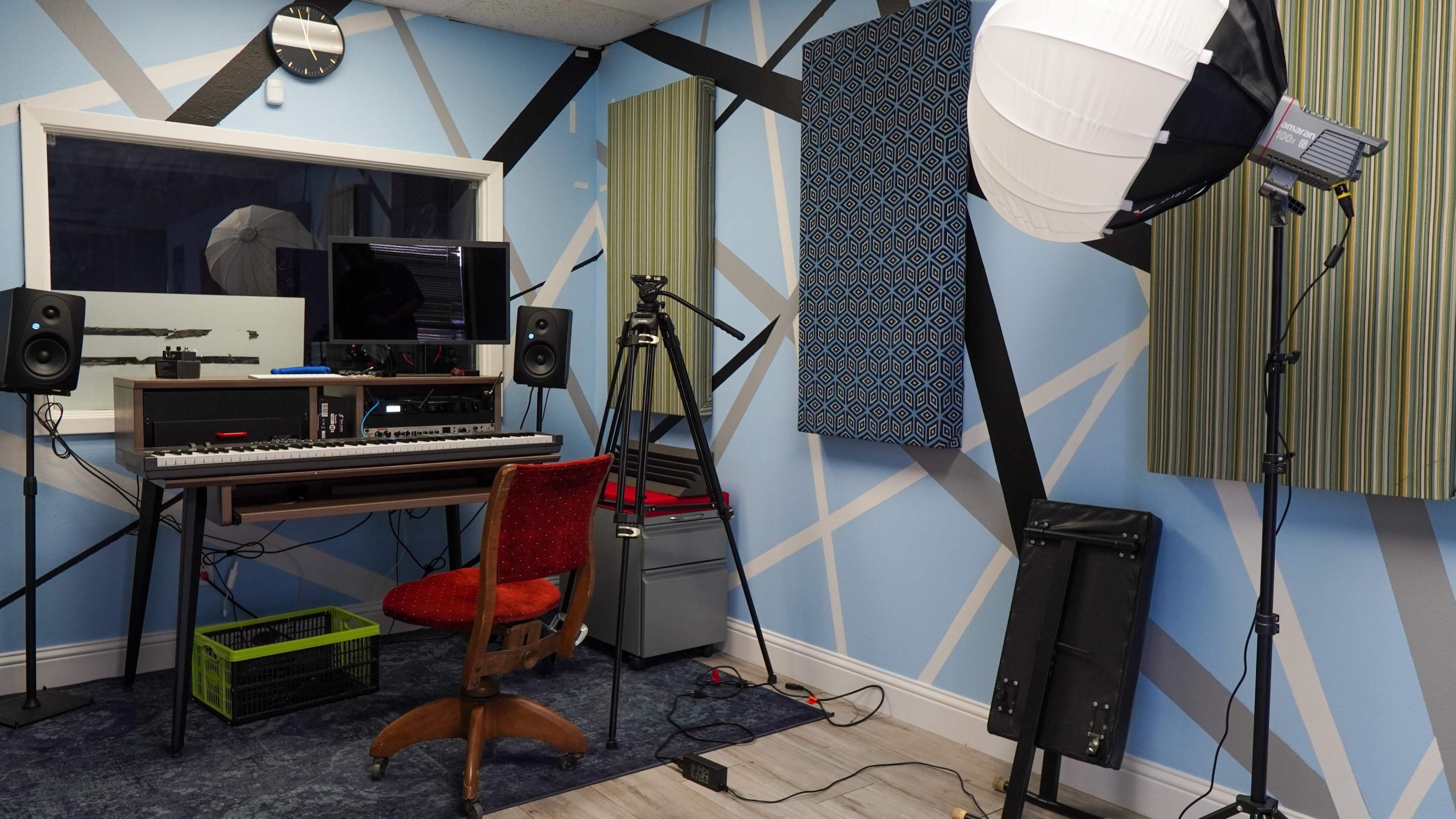 A small music or recording studio with a computer setup, microphone, and soundproofing panels on the walls.