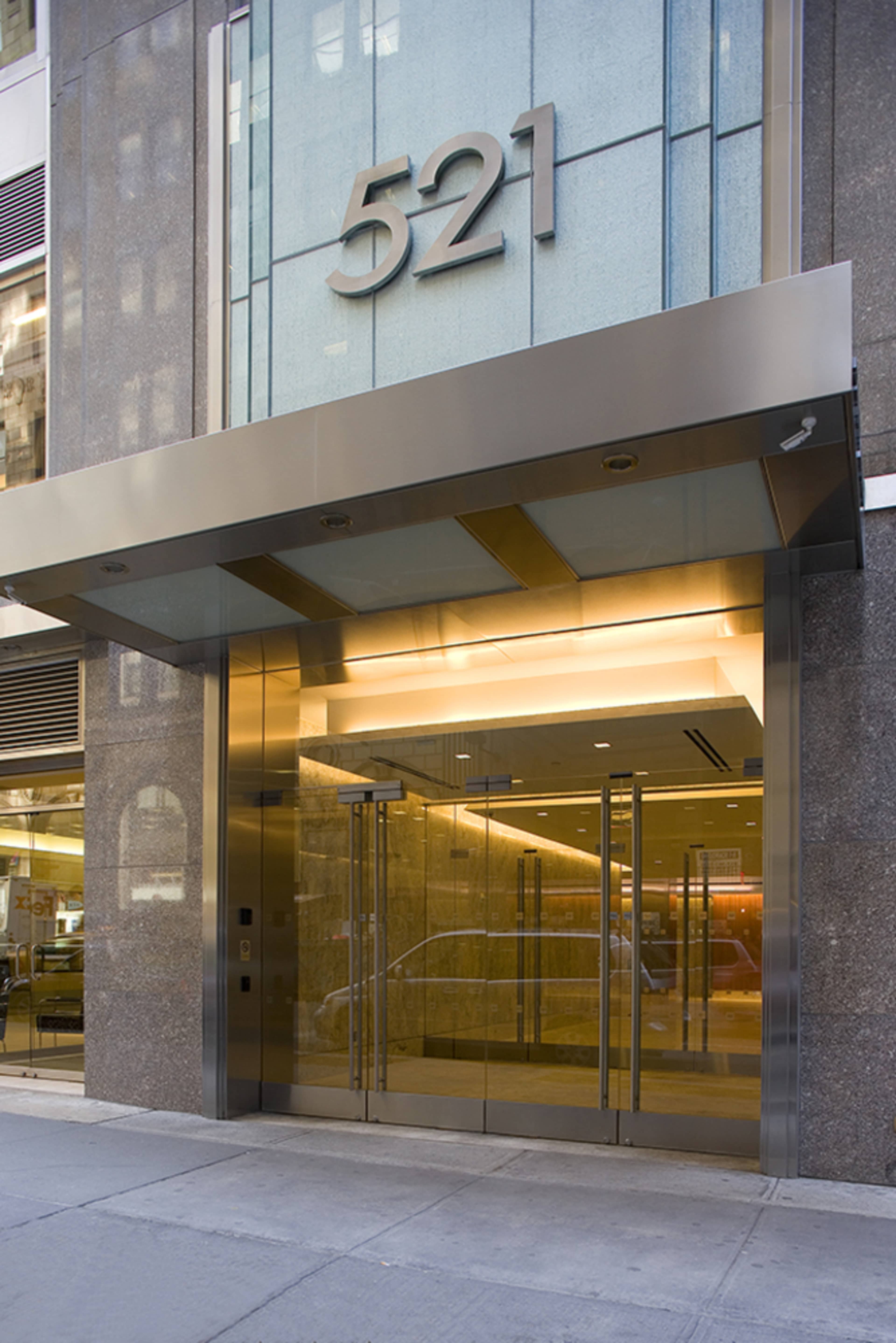 The image shows the entrance of a modern building with the number "521" prominently displayed above the glass doors.