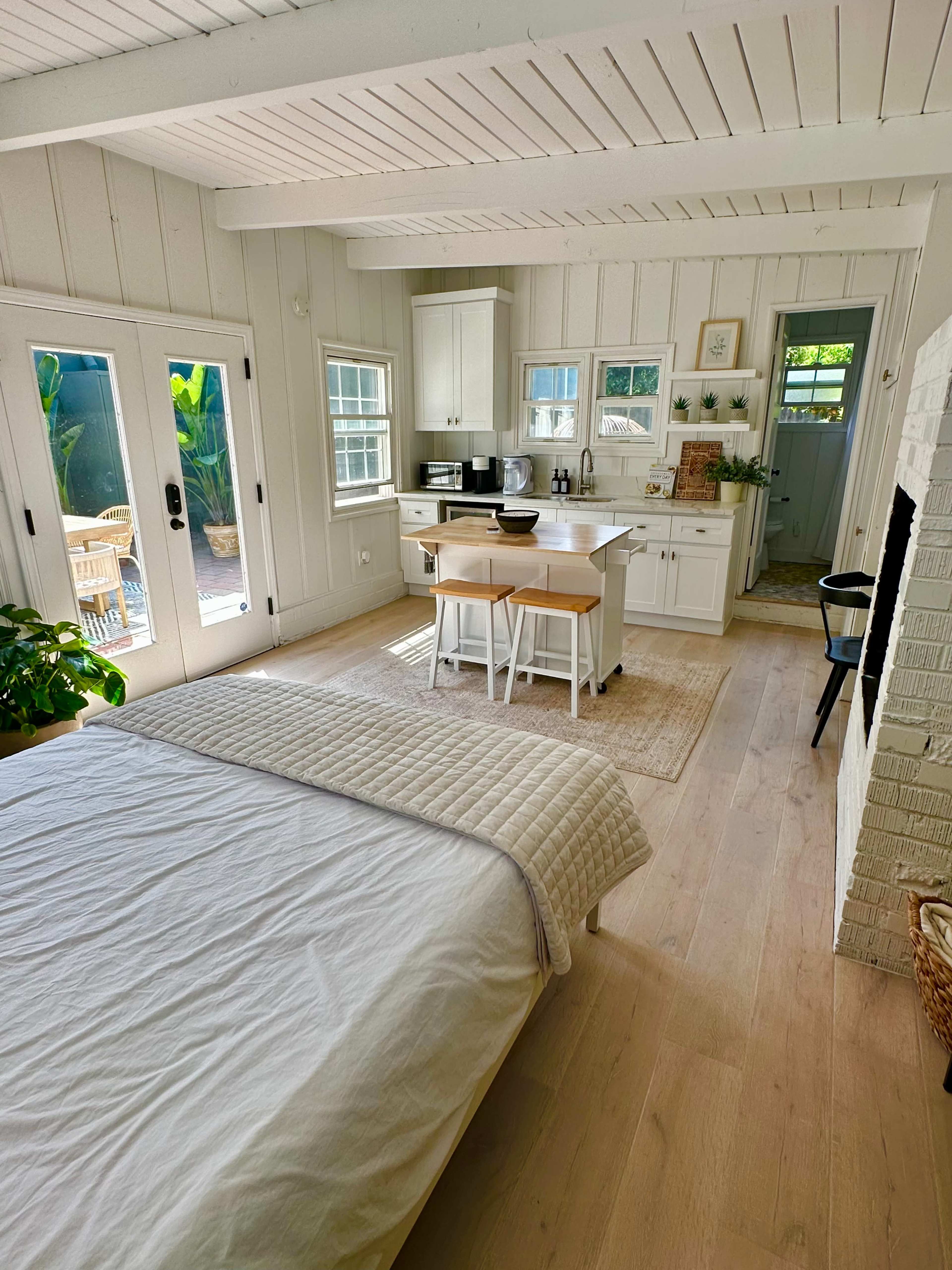 A bright, open-plan living space features a bedroom with a bed and a kitchenette area with a dining table and chairs.