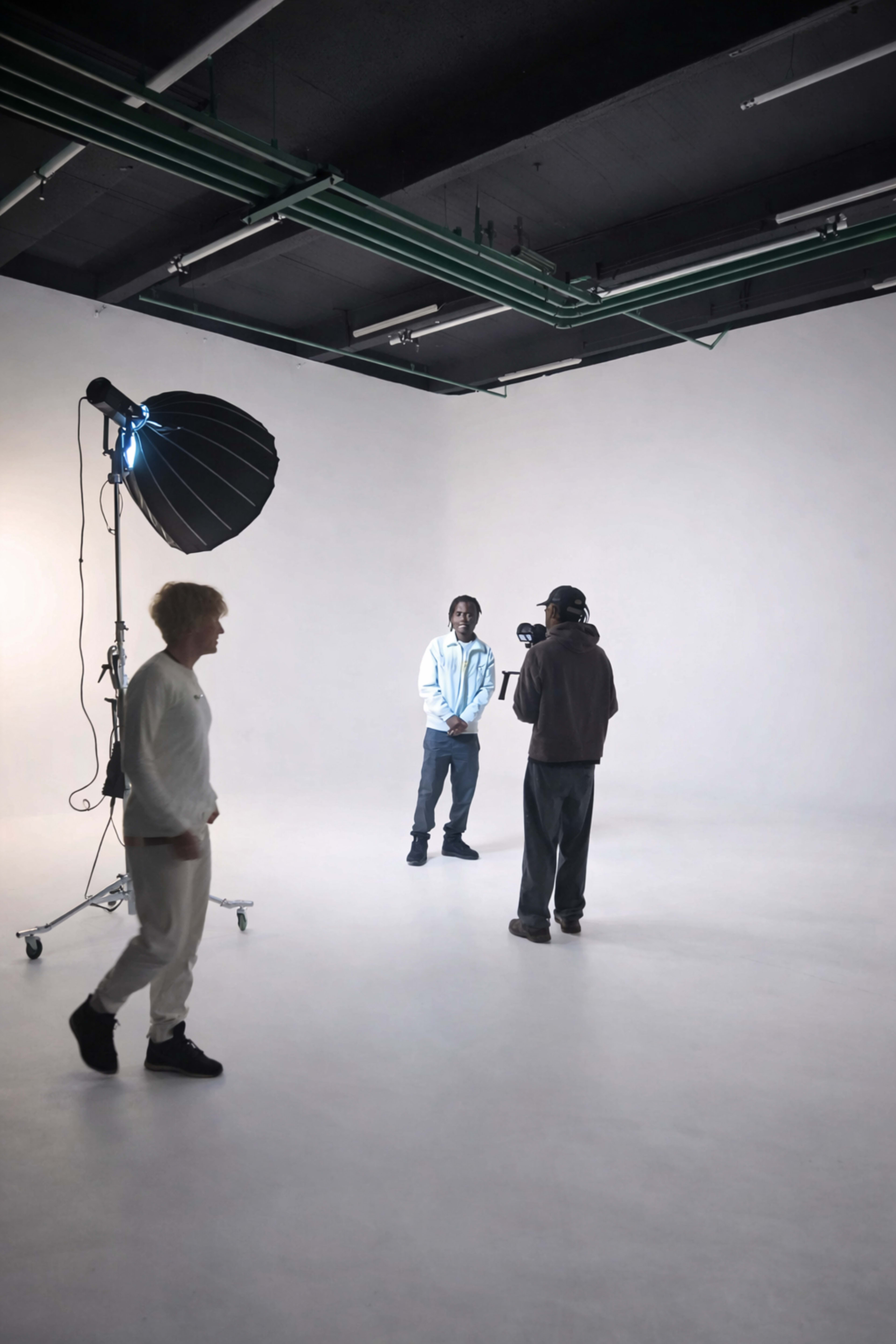 A photographer captures a portrait of a model in a studio with a large umbrella light and a simple white backdrop.