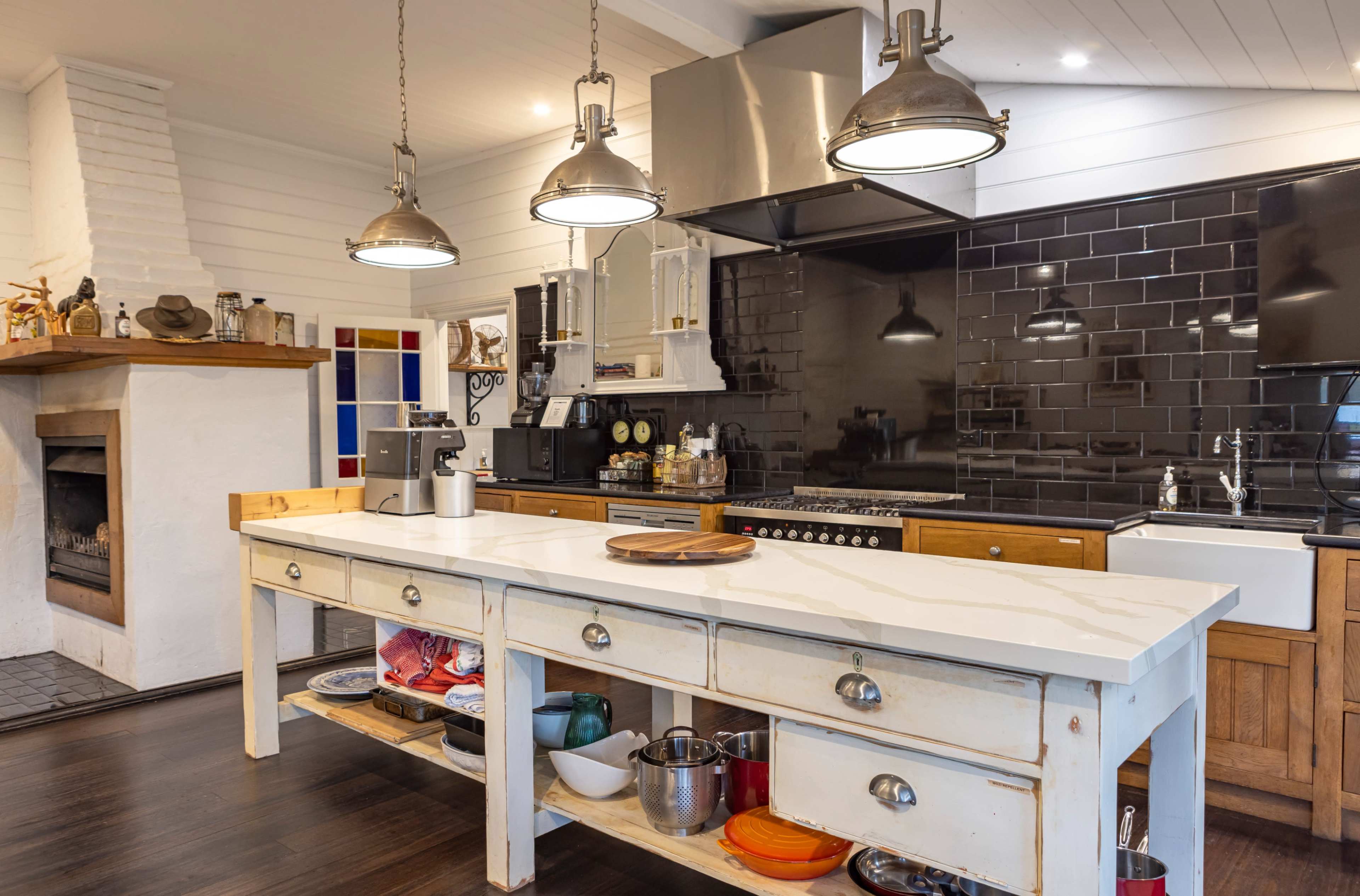 The image shows a modern kitchen featuring a central island with a white countertop, stainless steel appliances, and a fireplace in the background.