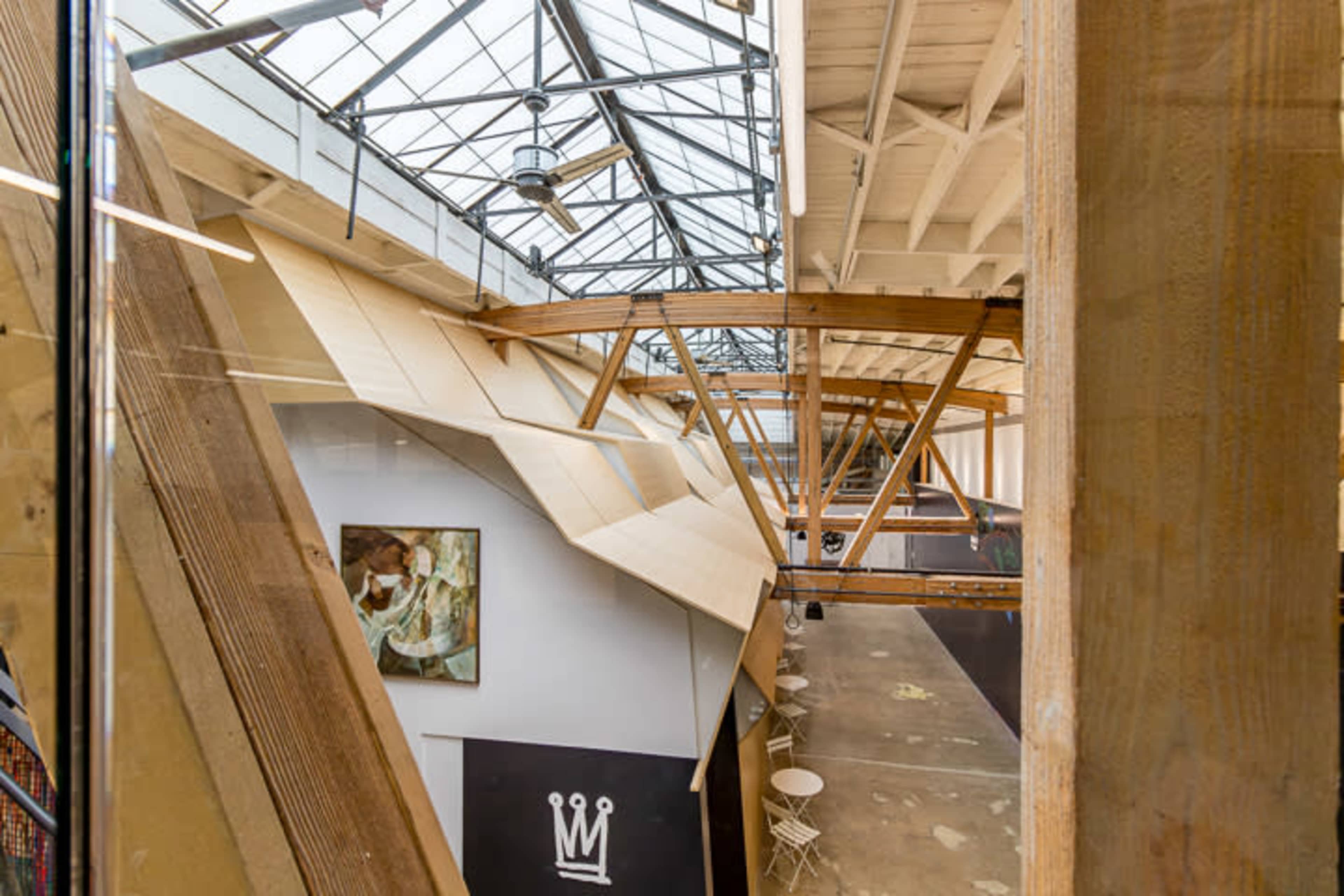An industrial space with wooden beams and an open layout, featuring large windows and a painting on the wall.