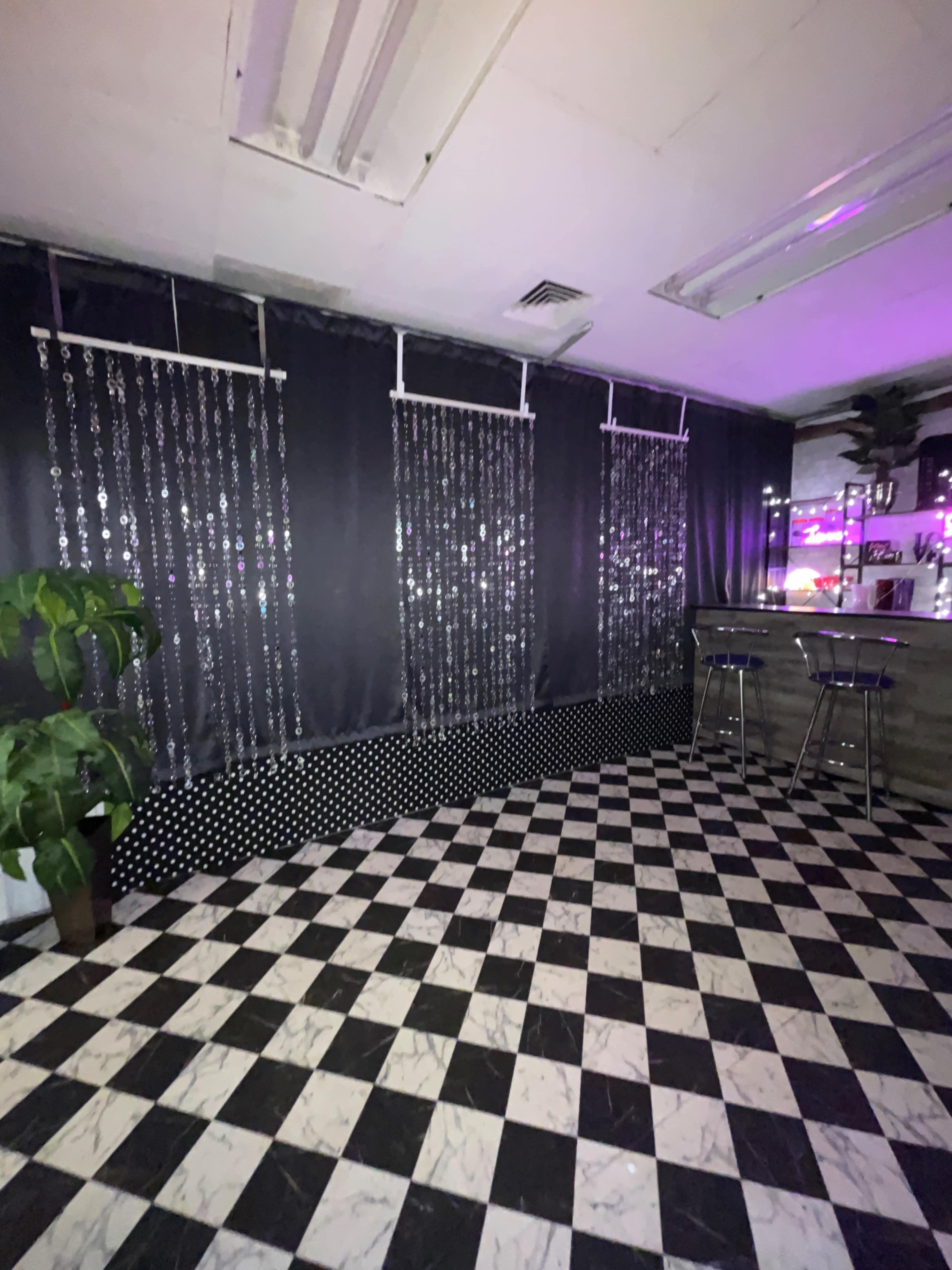 An interior space with a black and white checkered floor, two decorative curtains with sparkly beads, and a bar area with two stools.
