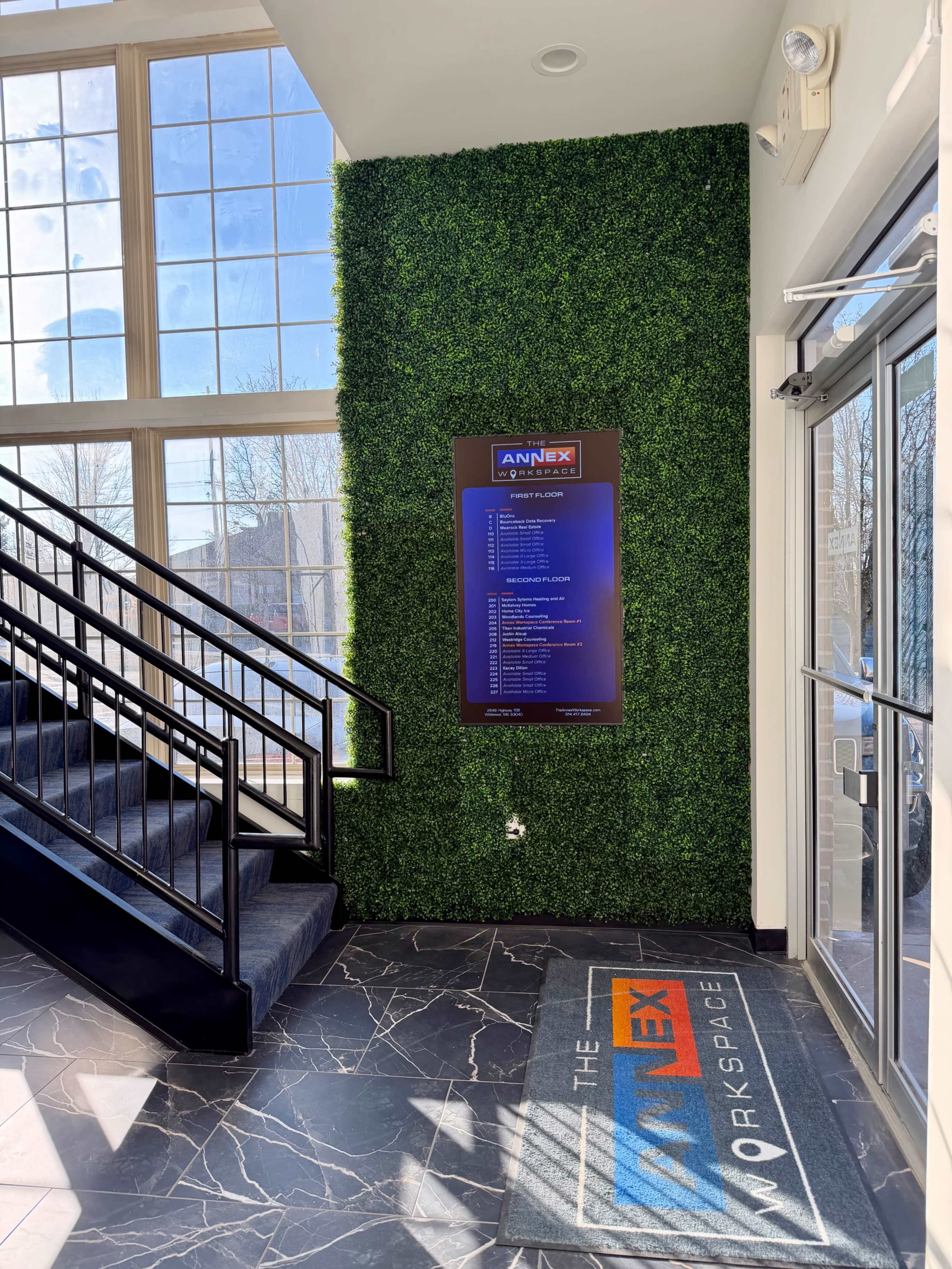The image shows an indoor entrance area with a green wall, a staircase, and a sign displaying a list of services or amenities for "The Annex Workspace."
