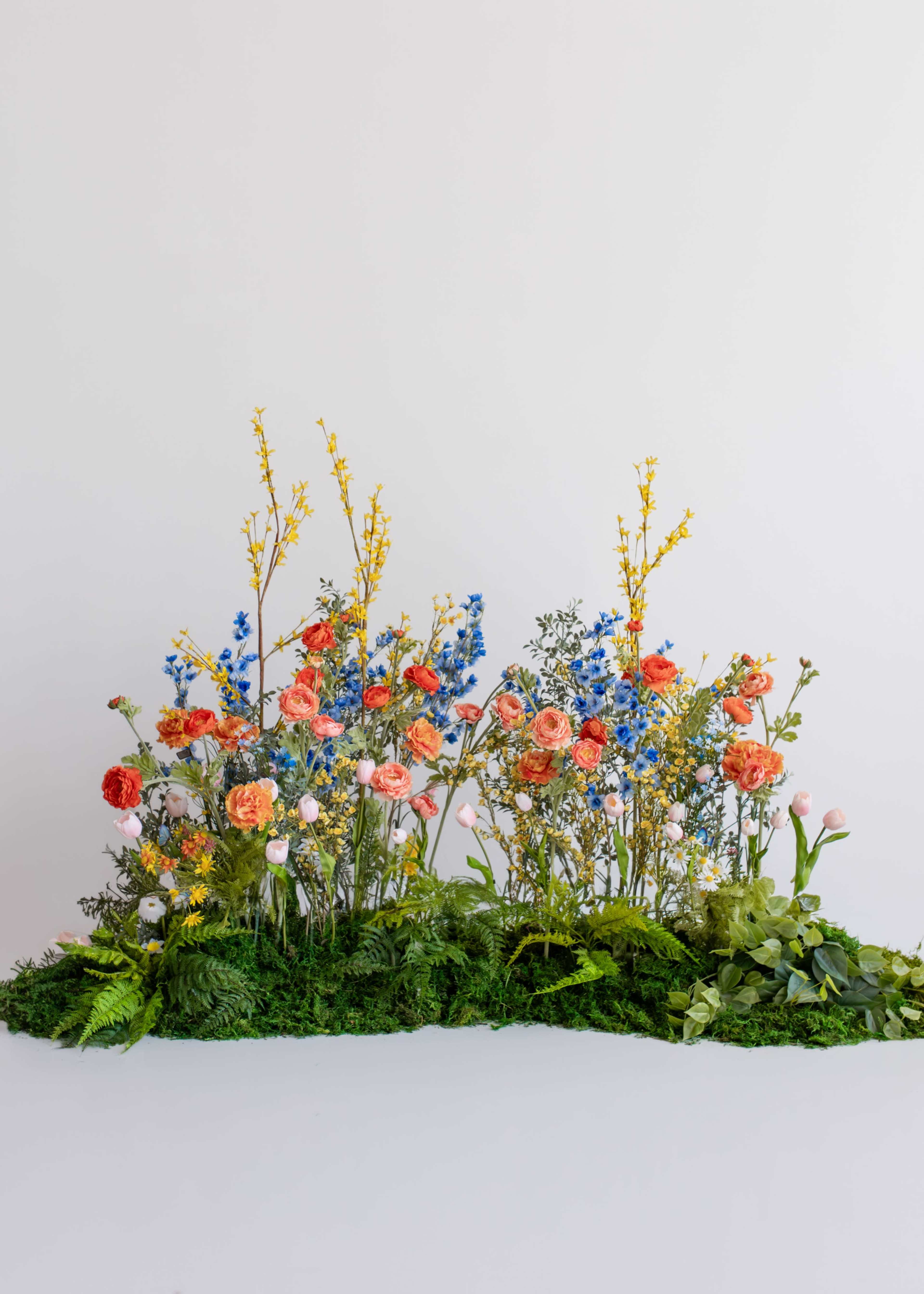 A vibrant arrangement of various flowers and greenery is displayed on a white background.